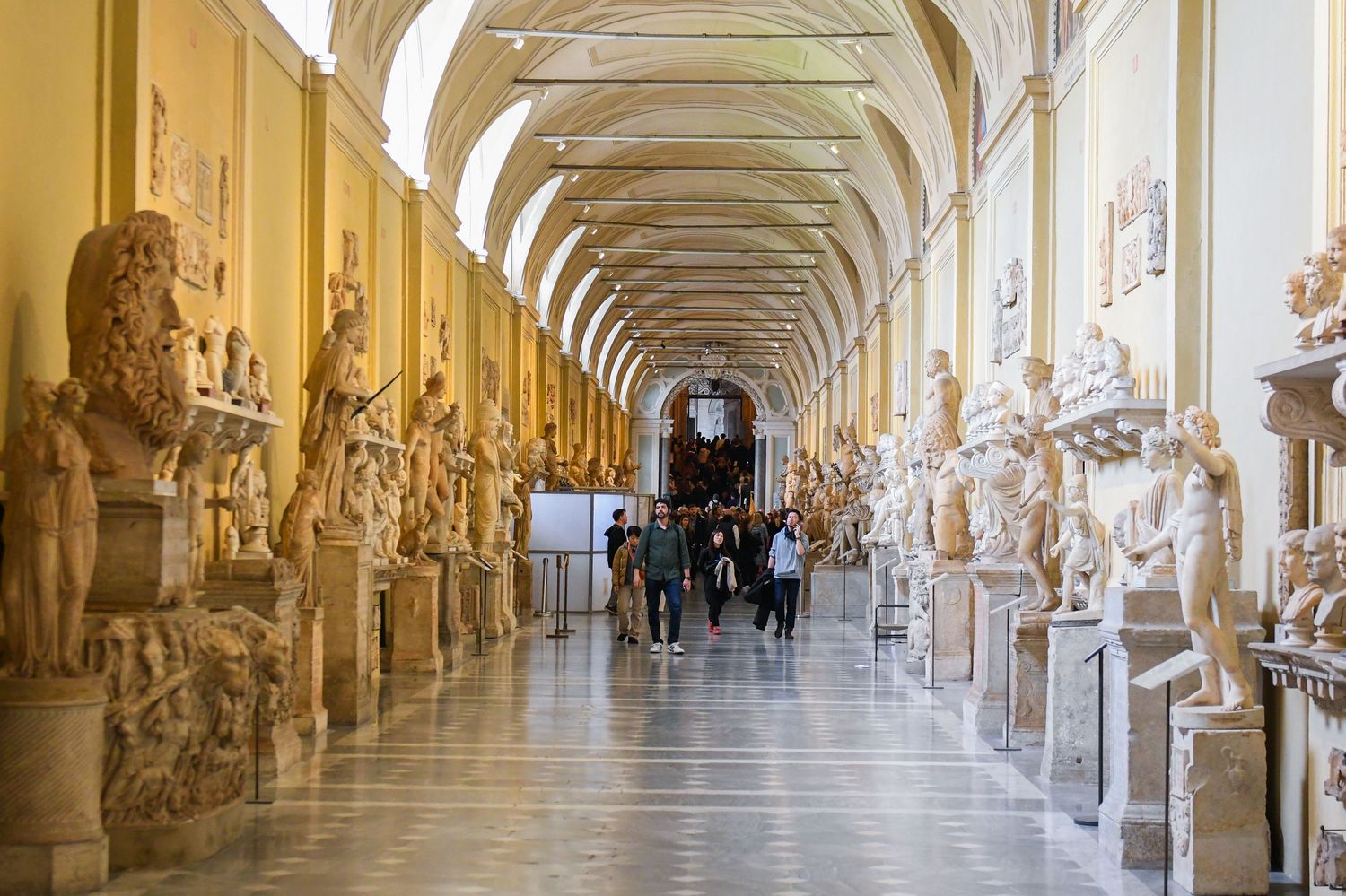 Elegant museum hallway with vaulted ceiling and marble statues lining both sides.