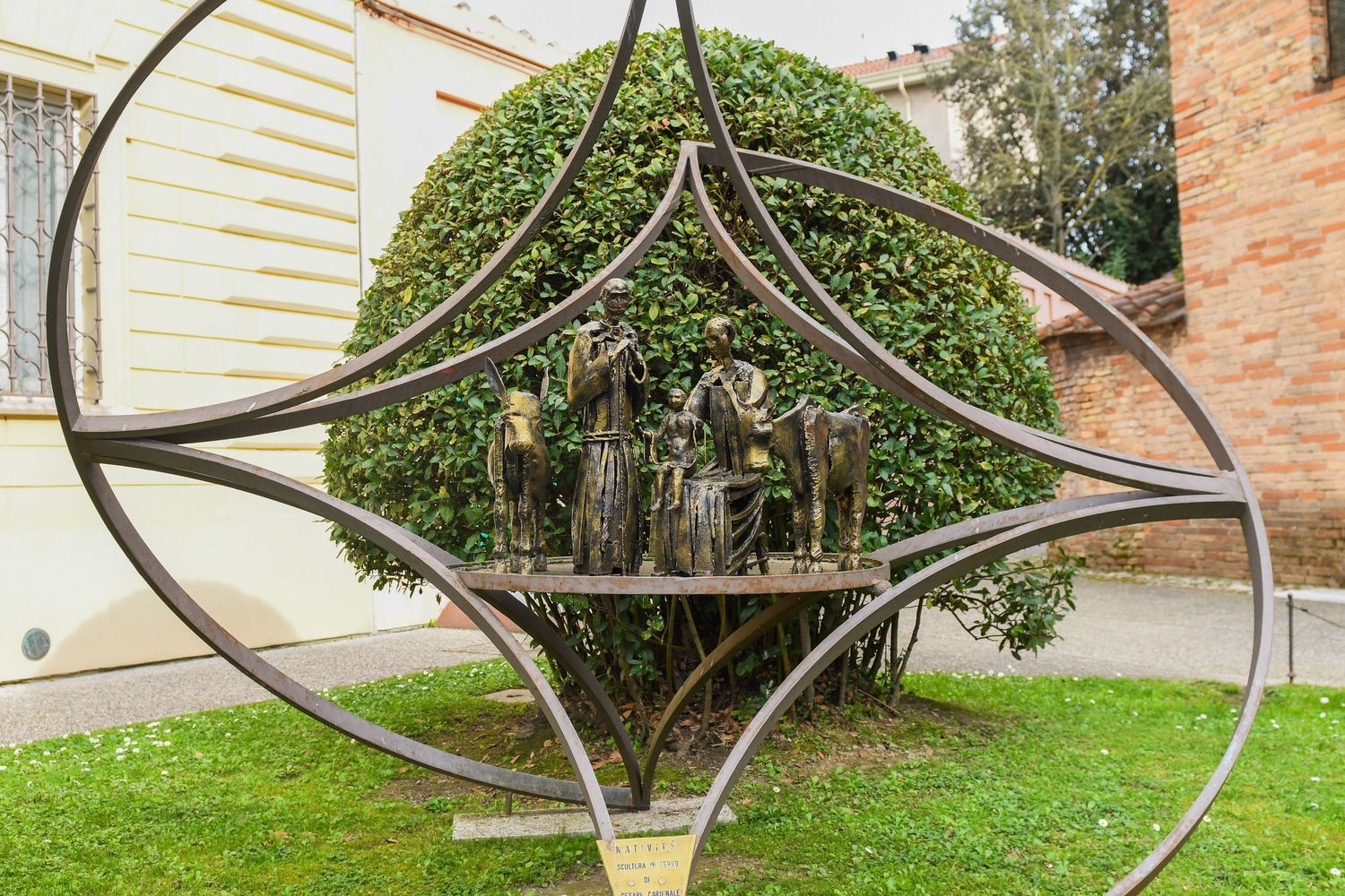Modern metal sculpture with circular geometric design stands in a garden setting.