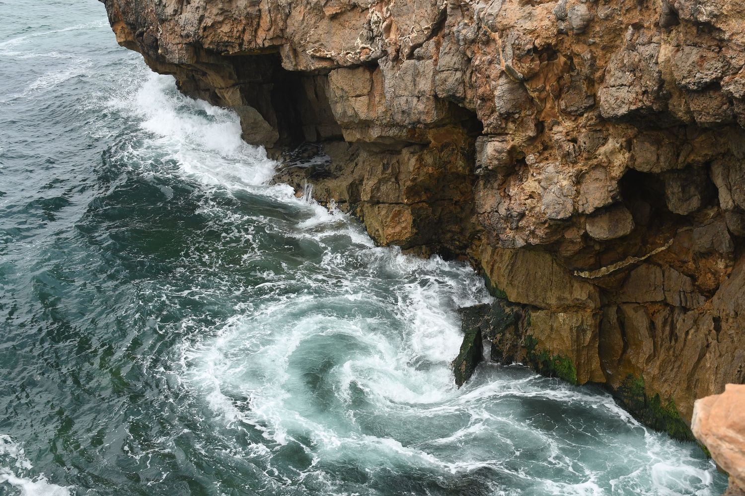 Aerial view of rugged coastal cliffs with crashing ocean waves against rocky shoreline during stormy weather.