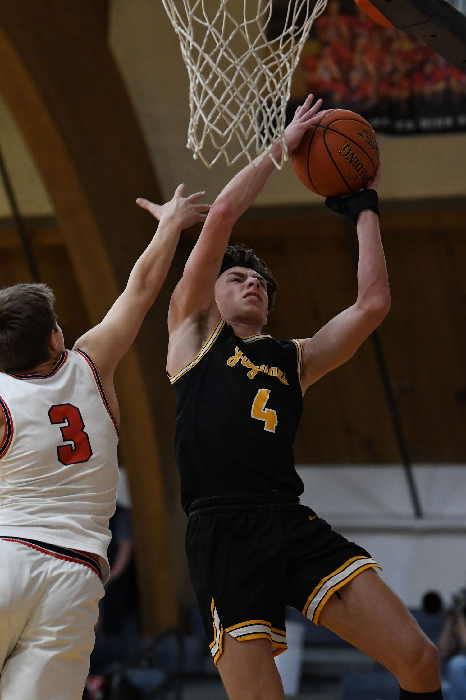 Player in black jersey attempts layup while being defended under basket.