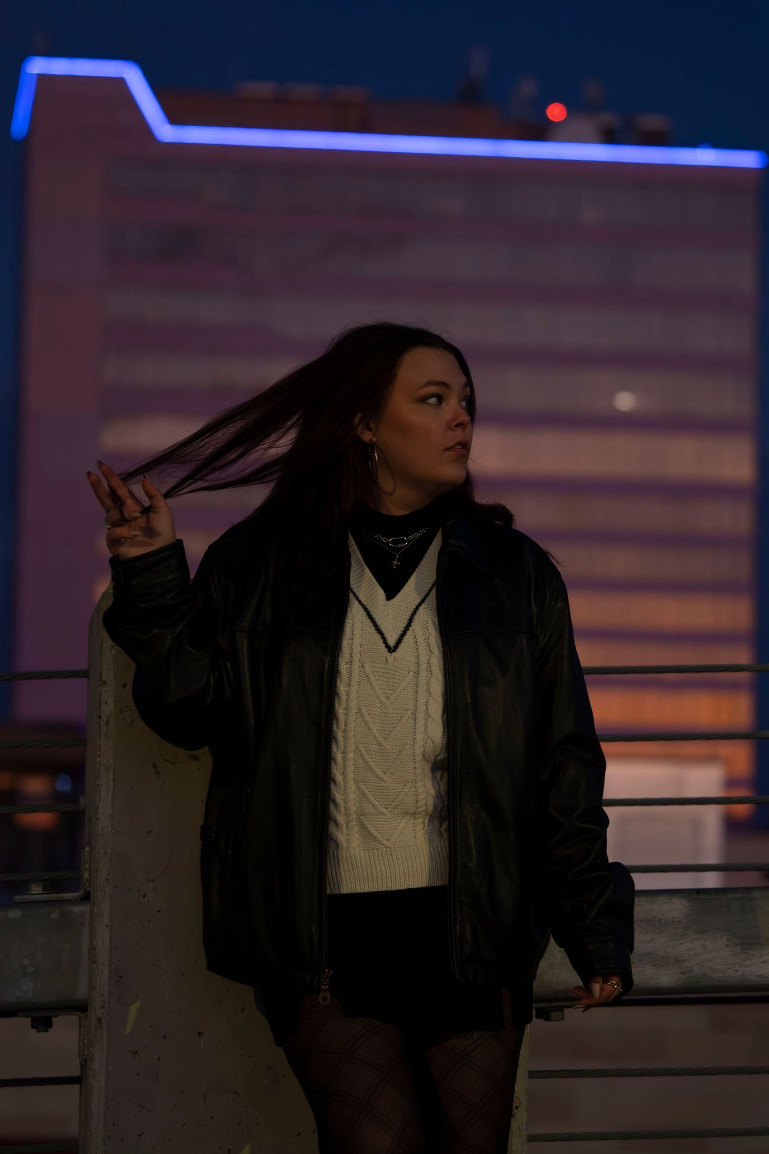 Dark moody portrait of someone in winter attire against neon lights and sunset colors.