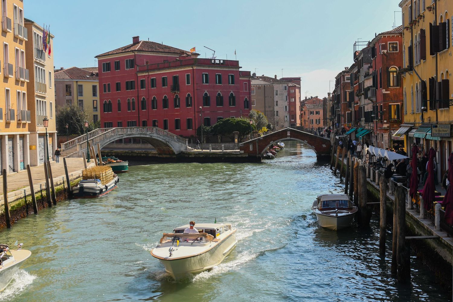 Speedboat cruises through a Venice canal under stone bridges with colorful buildings lining the waterway.