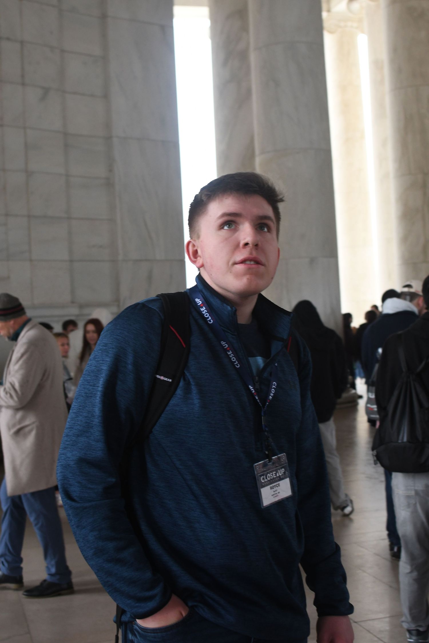 Person wearing a blue sweater and lanyard stands between marble columns at a public building.