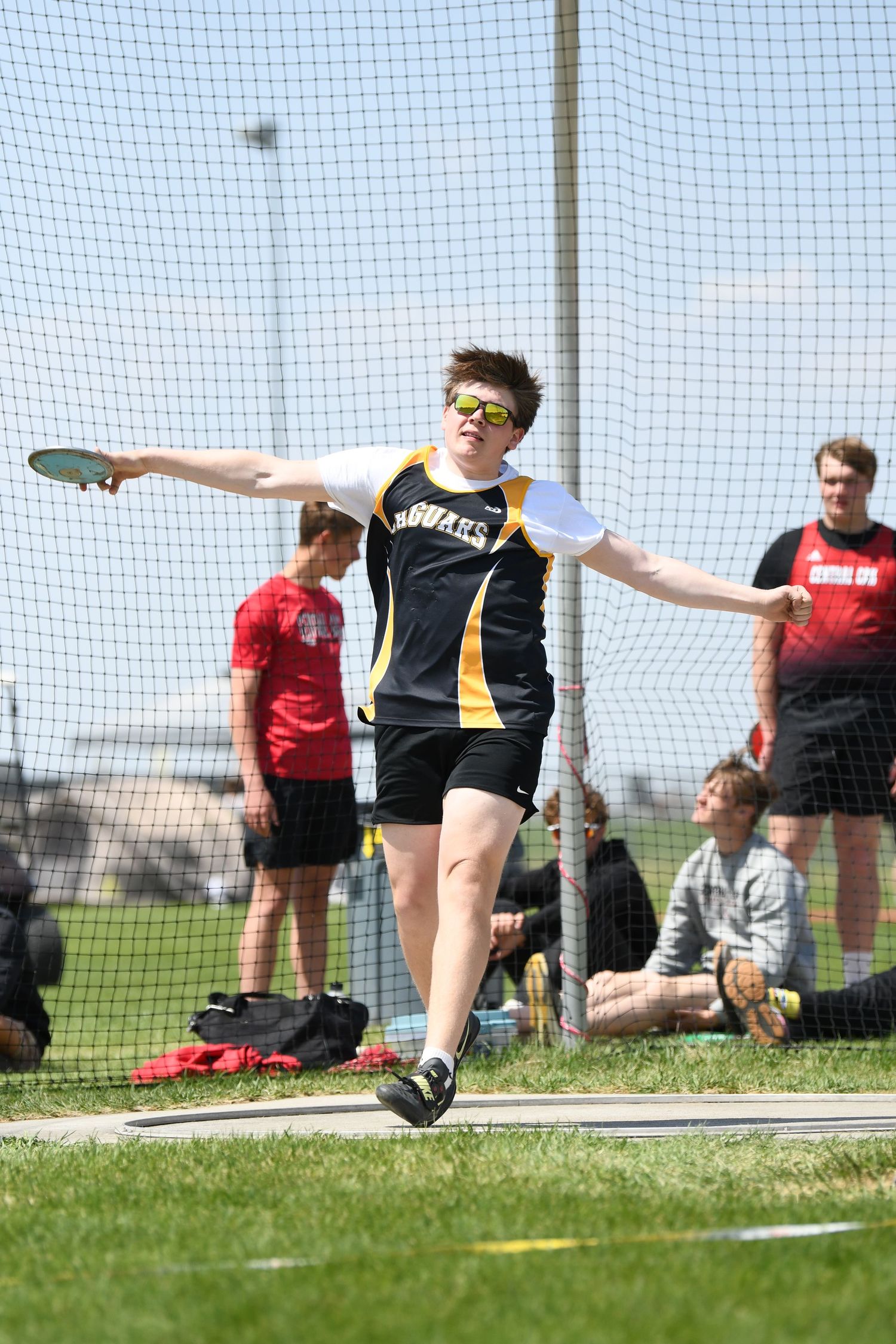 Track athlete in black uniform releases discus during outdoor competition.