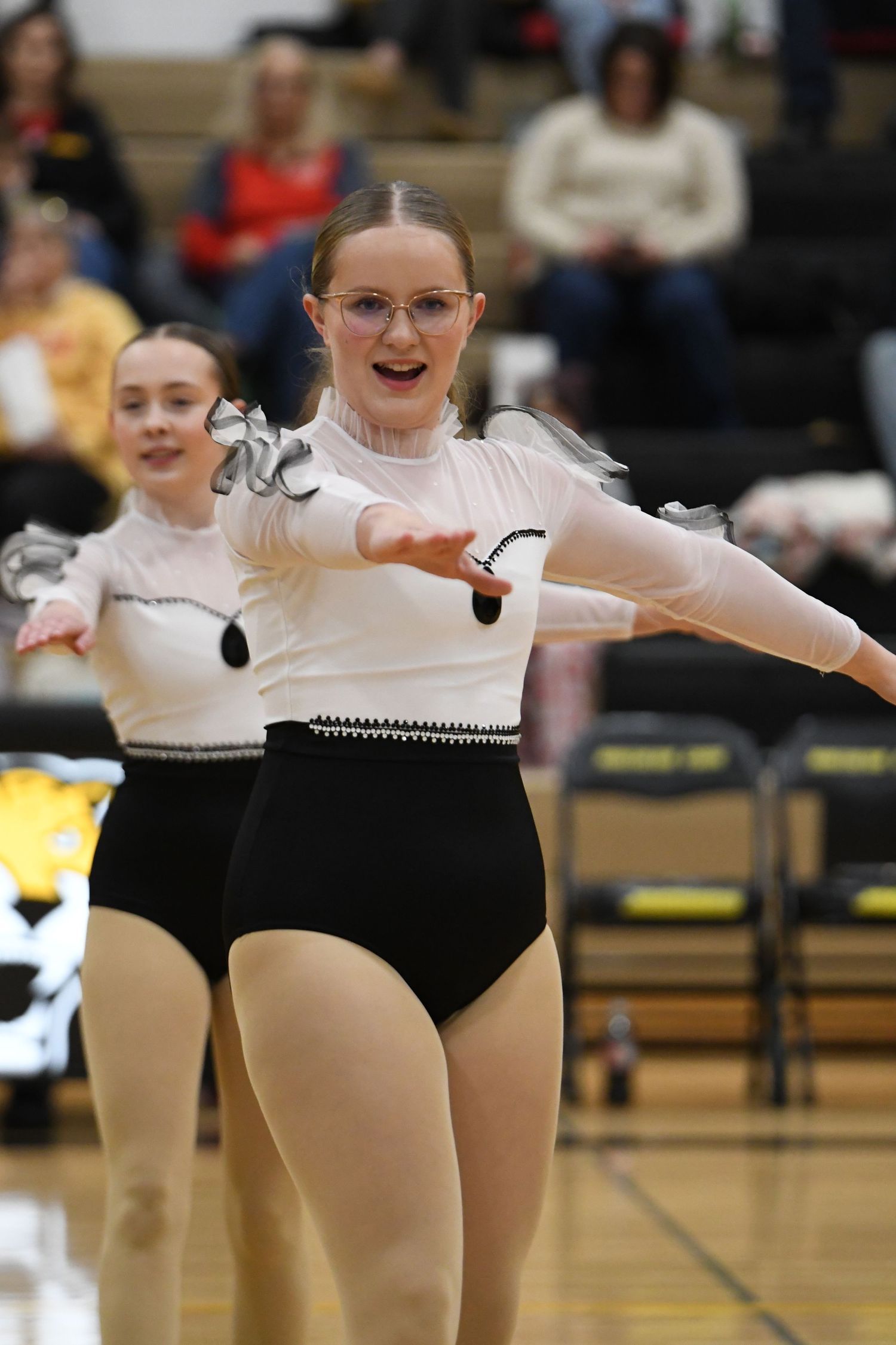 Dancer in black and white costume with glasses performs routine in school gymnasium.