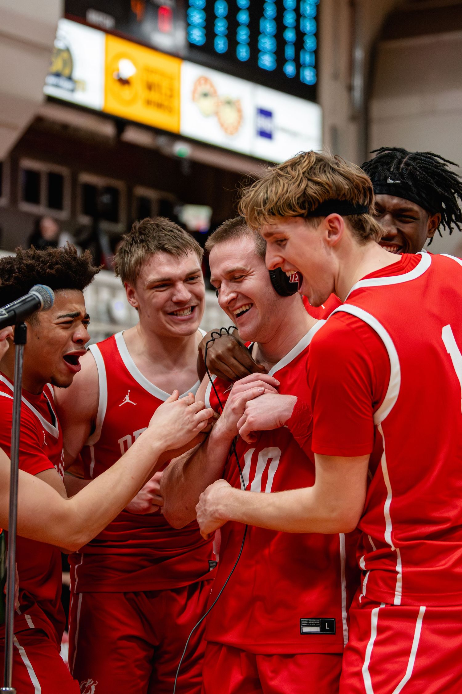 Basketball players in red uniforms celebrate together near a microphone after a winning game.