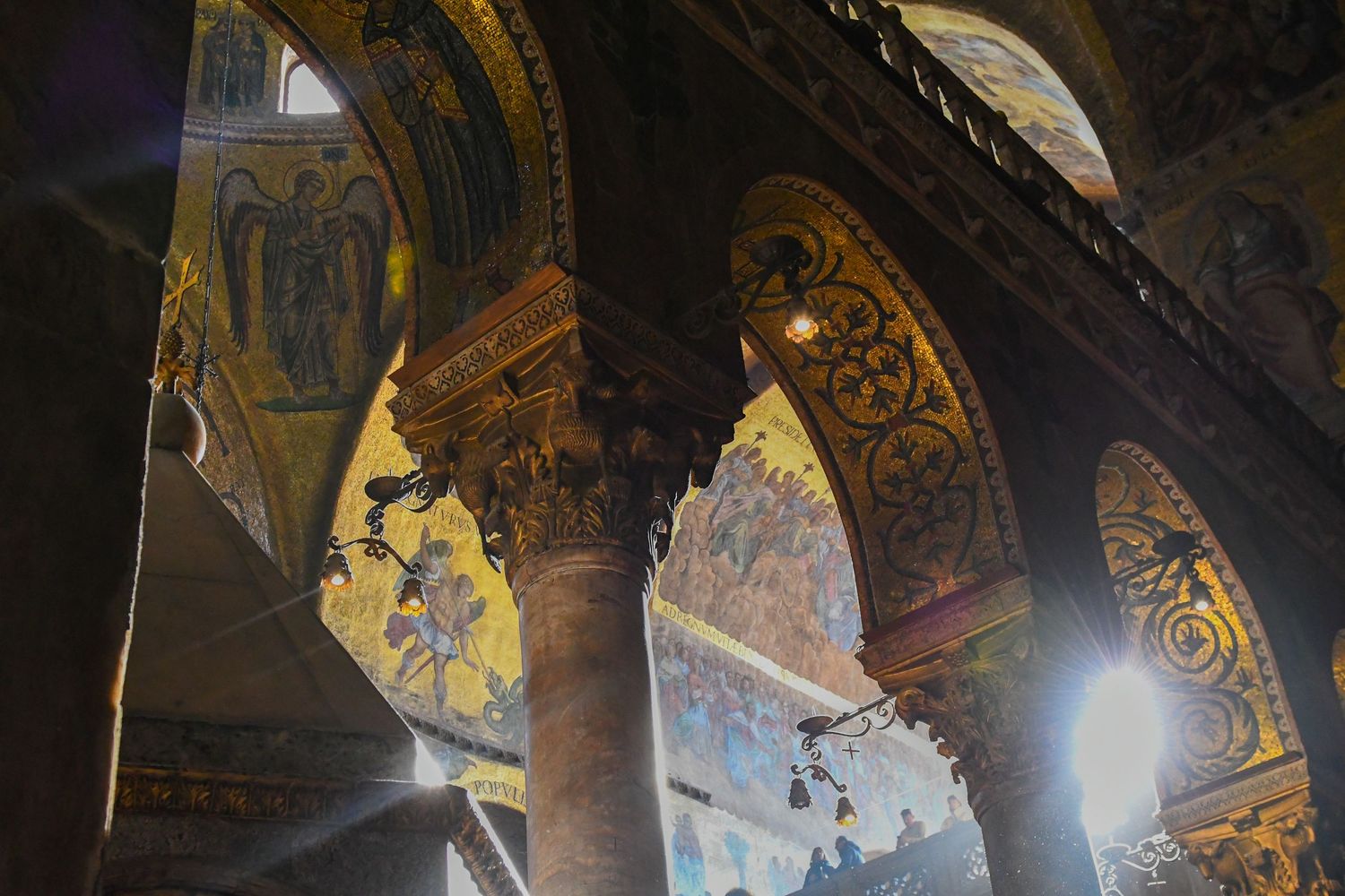 Ancient church ceiling with ornate golden mosaics and religious artwork illuminated by dramatic lighting.