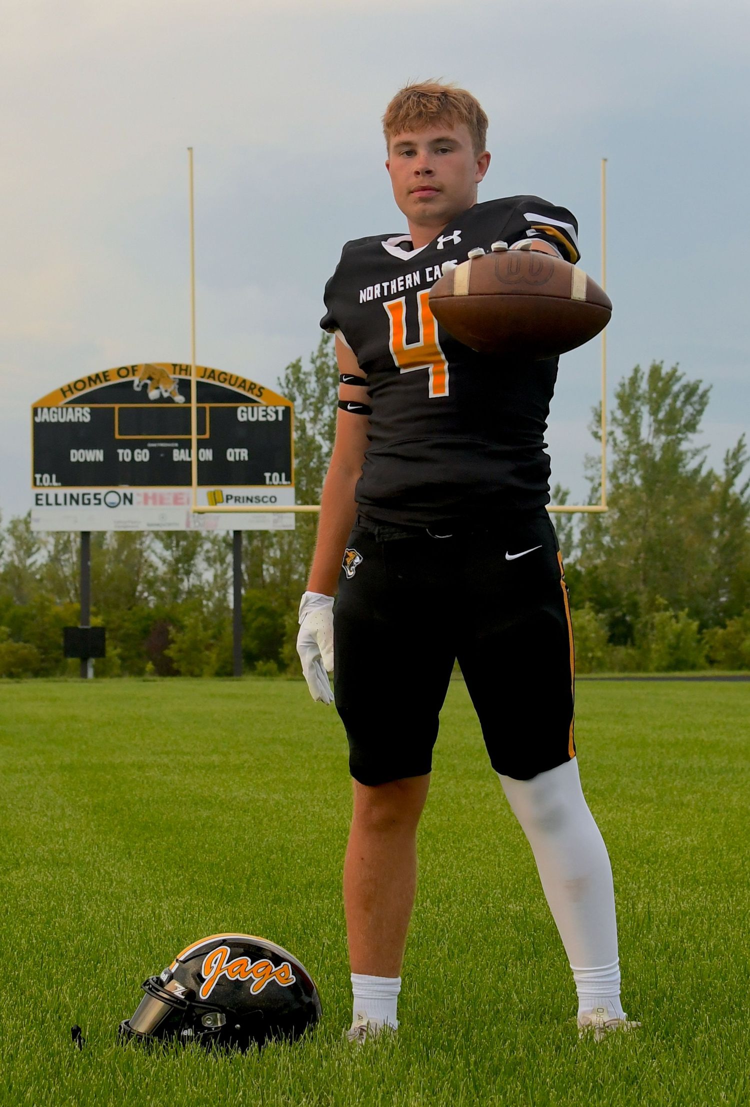 Football player in black uniform photographed from waist down on grass field.