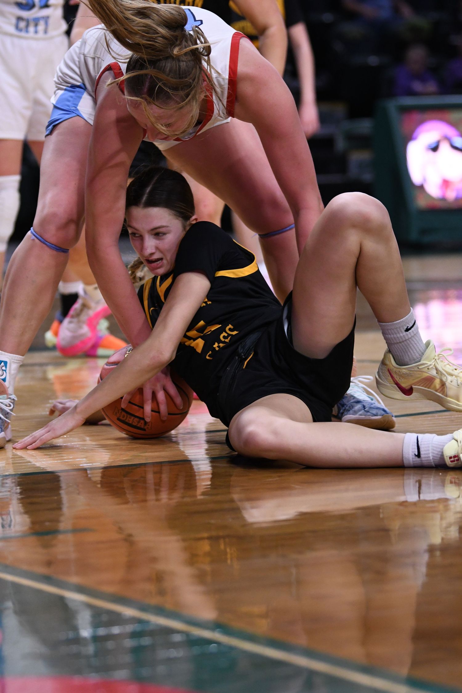 Players dive for loose basketball on wooden court floor.