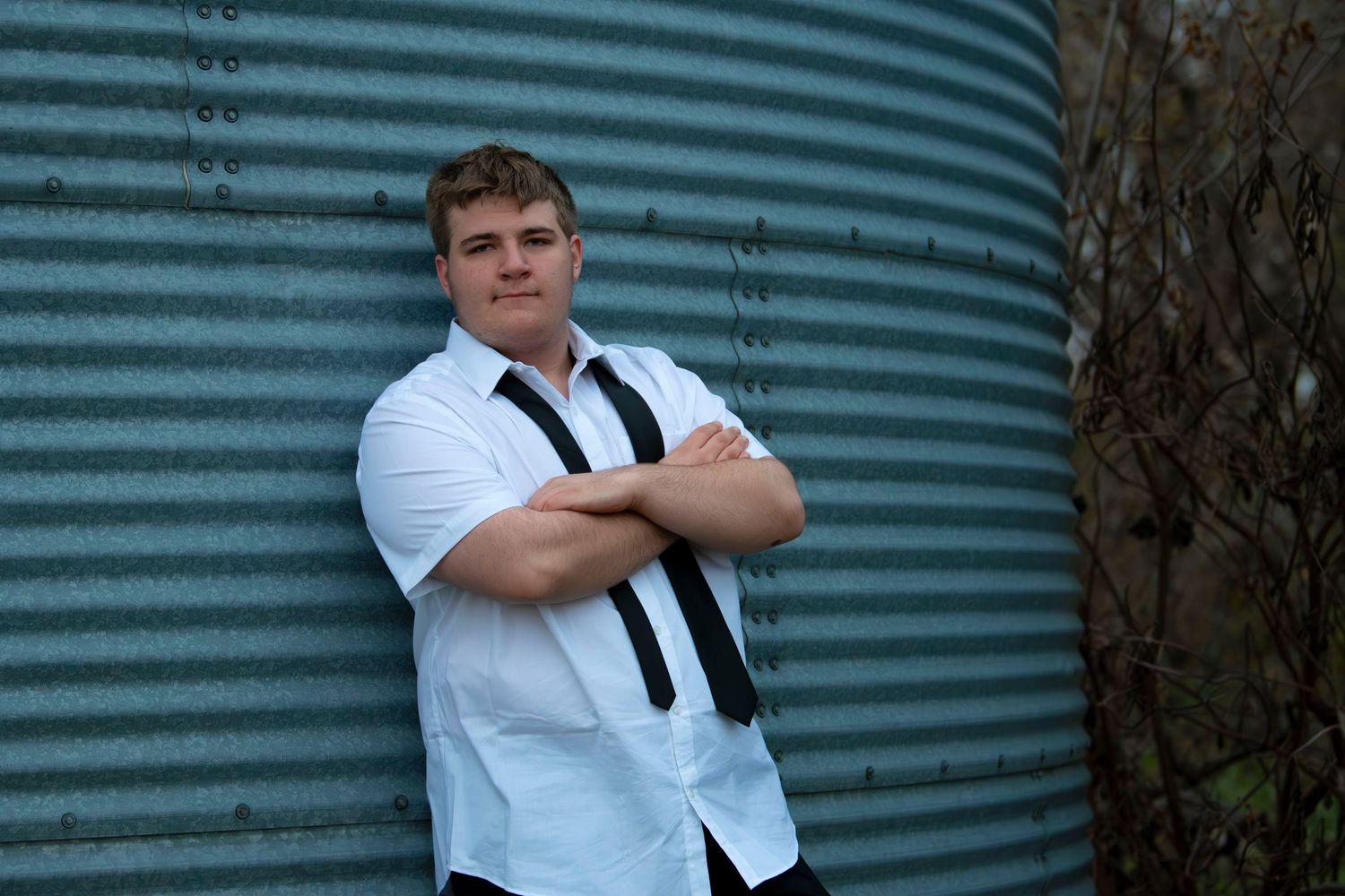 A figure in formal white shirt and black tie poses against a curved metal wall in four similar poses.
