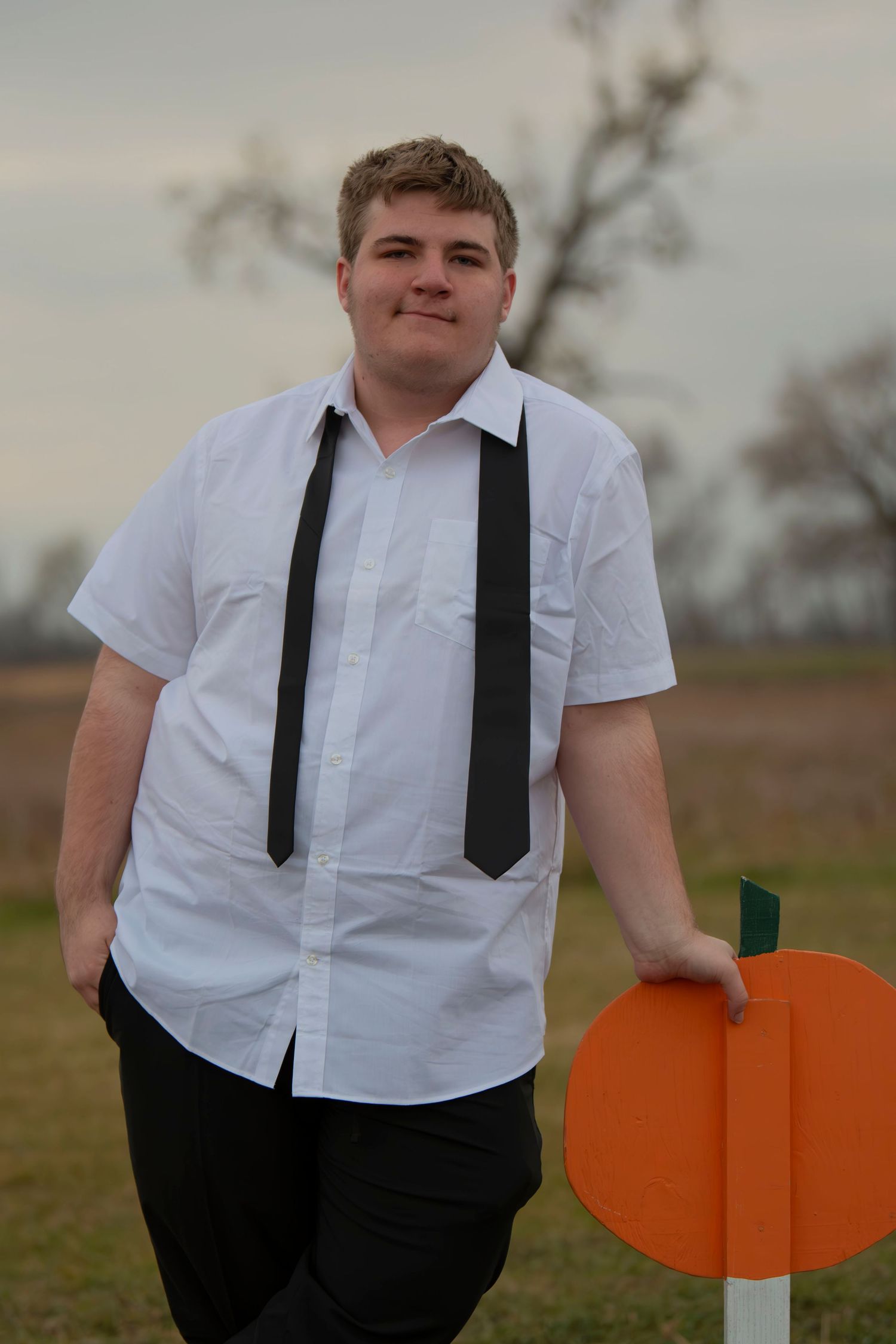 A person in a white button-down shirt and black suspenders stands in a field holding orange paper heart cutouts.