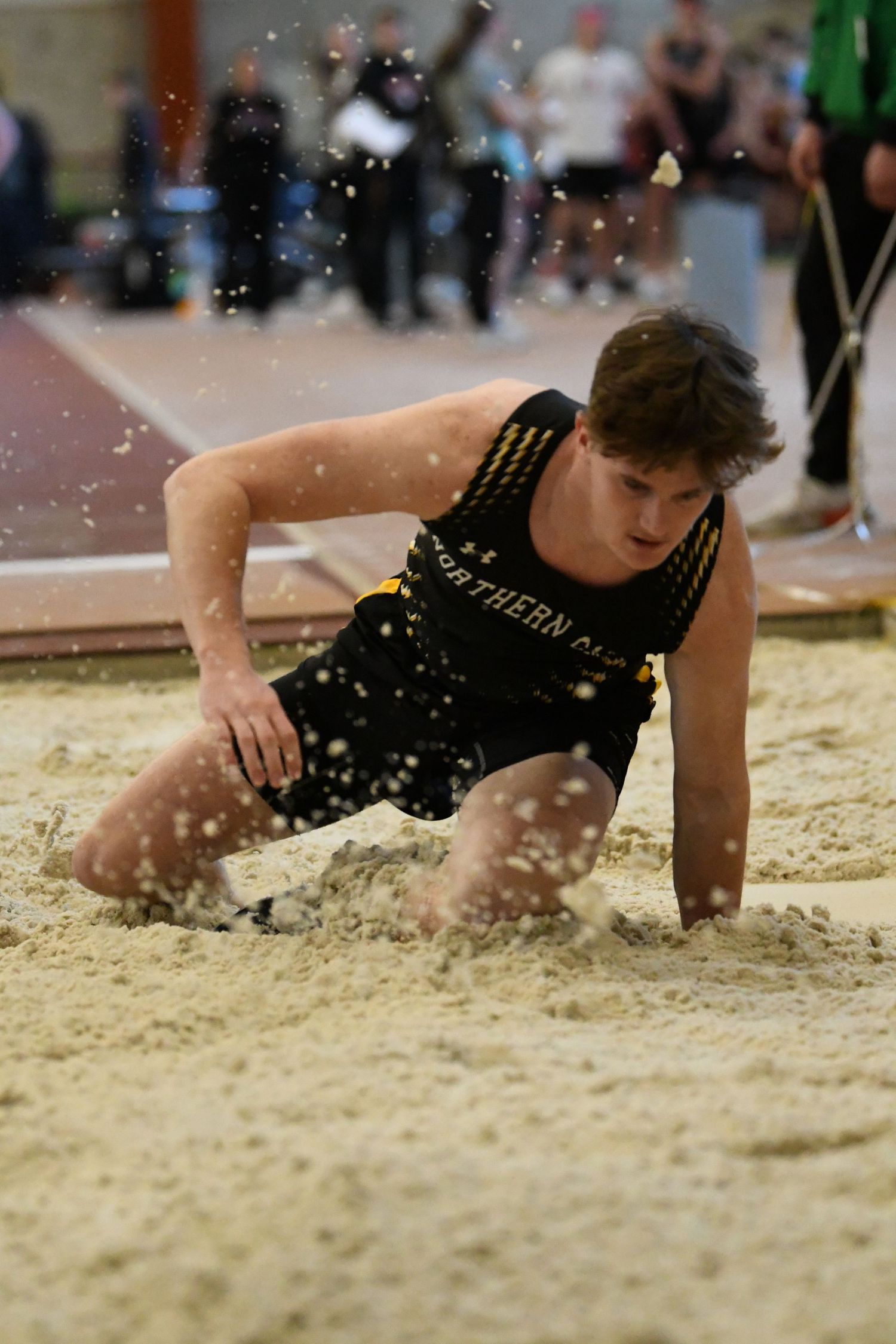 An athlete performs a long jump landing in the indoor sand pit during a track meet.
