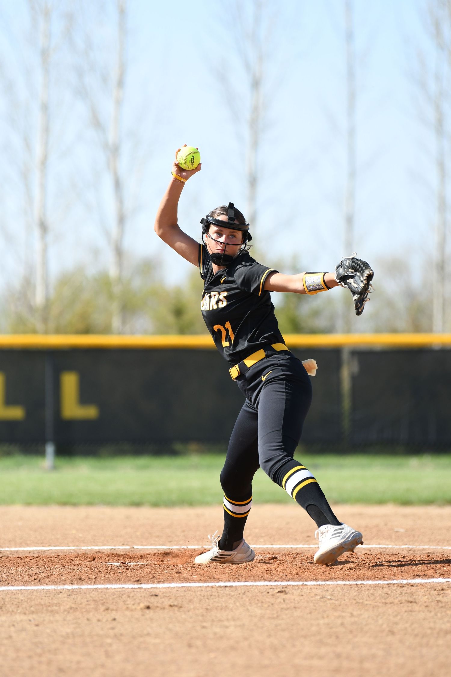 Softball player in black uniform dives and slides across infield dirt during defensive play.