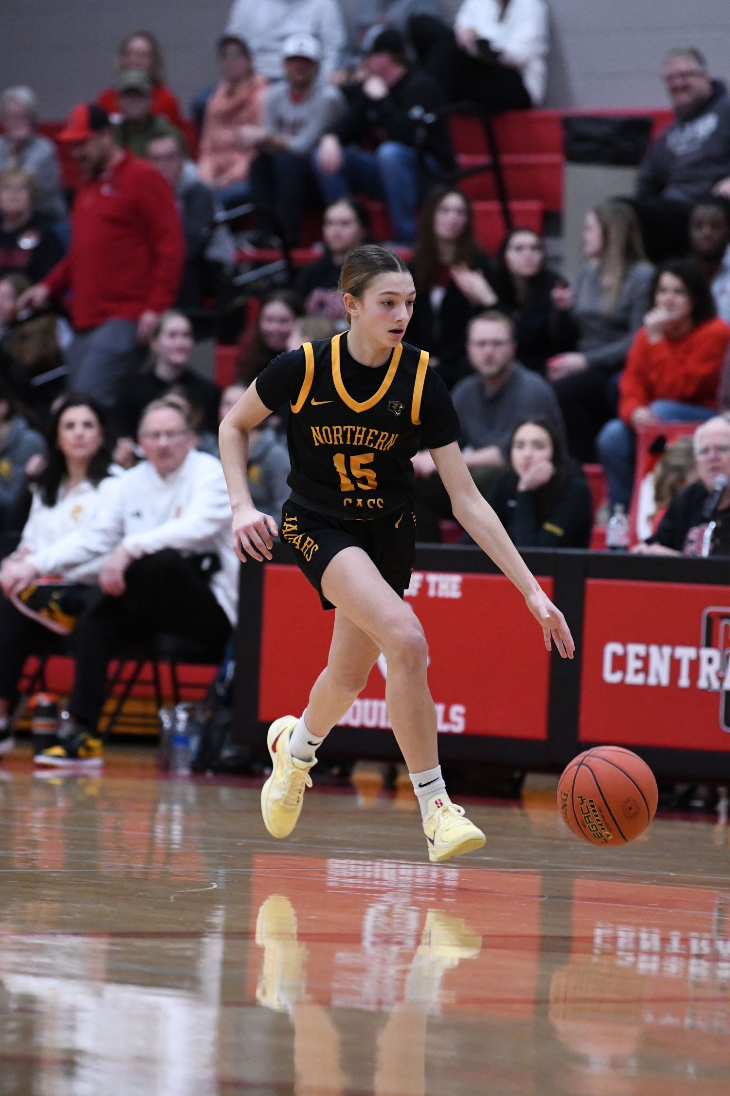 Player in black and gold uniform dribbles basketball on shiny court during game.
