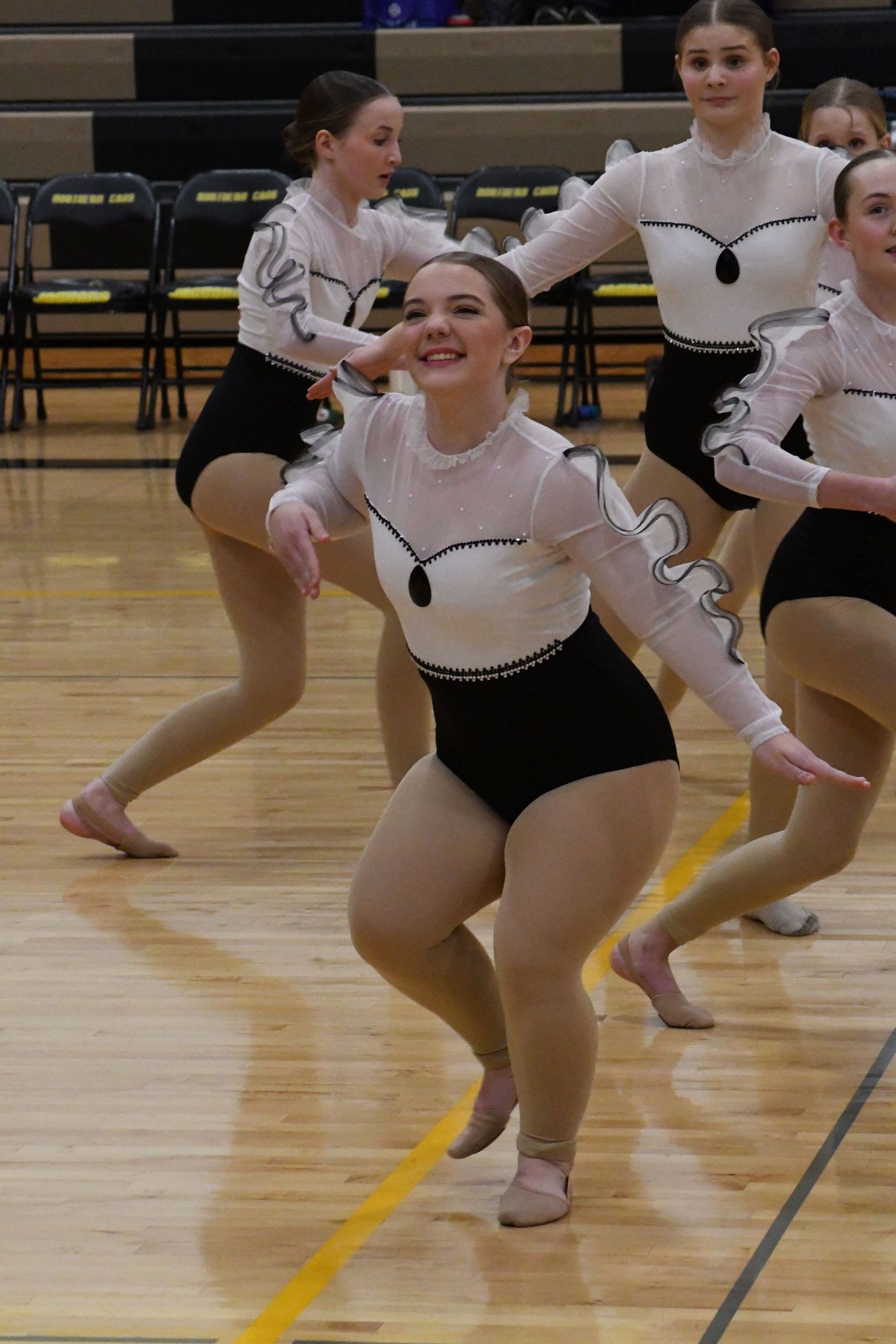 Dance team performers in black and white costumes execute a synchronized routine on a gymnasium floor.