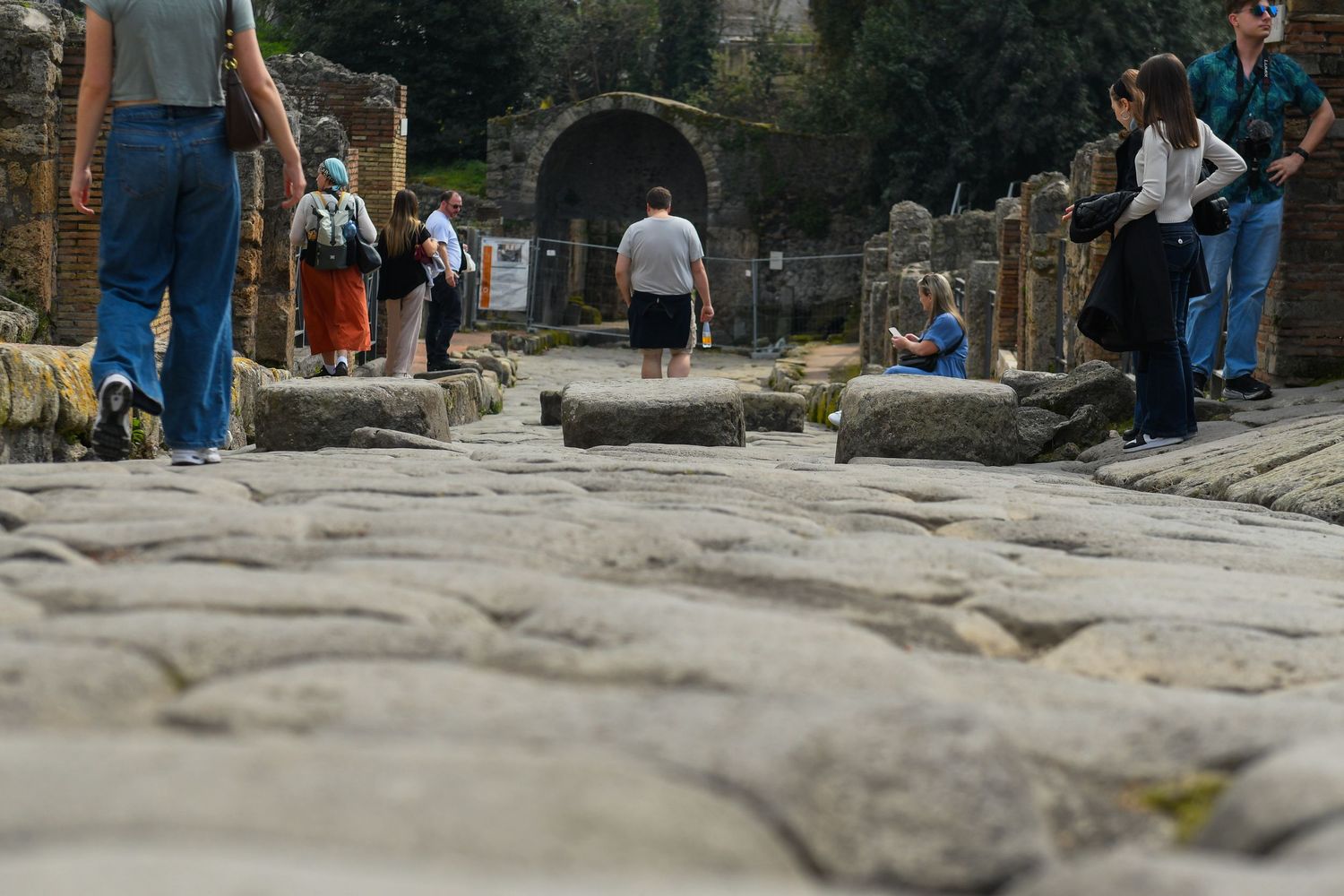 Ancient cobblestone street in Pompeii with tourists walking on the historic stones.