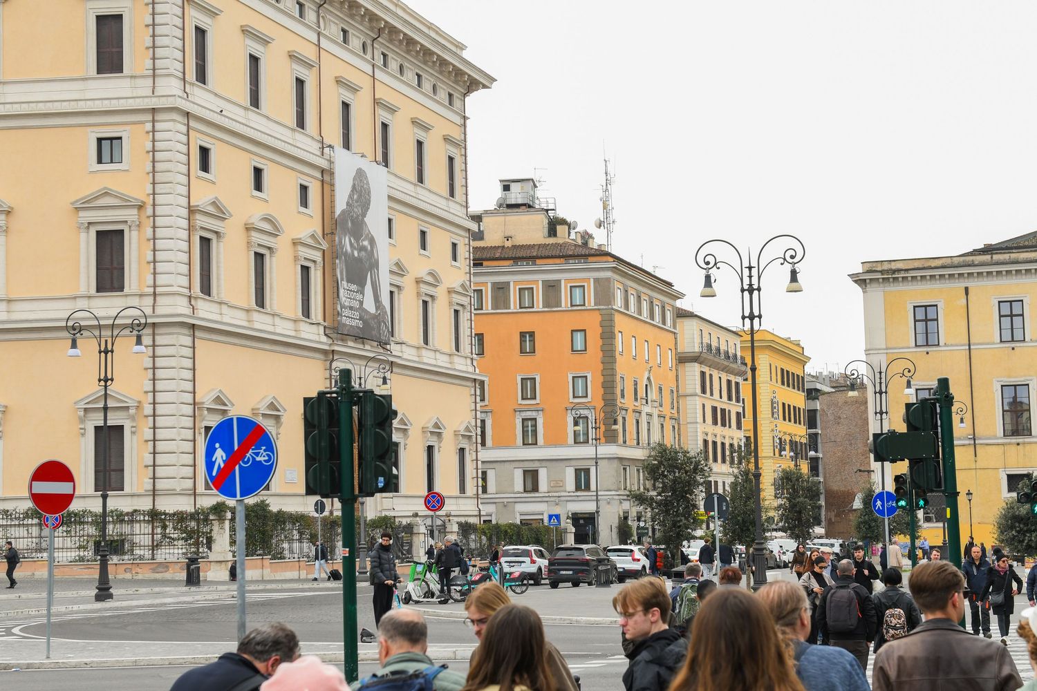 Busy street scene in Rome with historic yellow buildings and pedestrians walking along sidewalks.