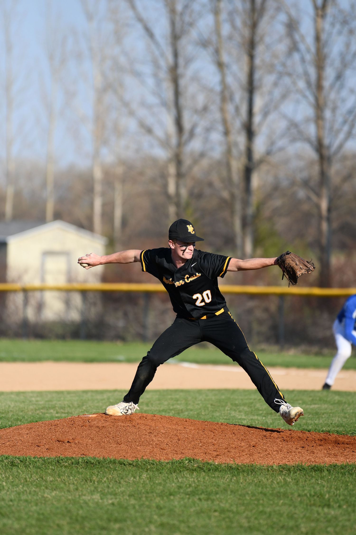 Pitcher in black uniform mid-delivery on baseball mound during game.