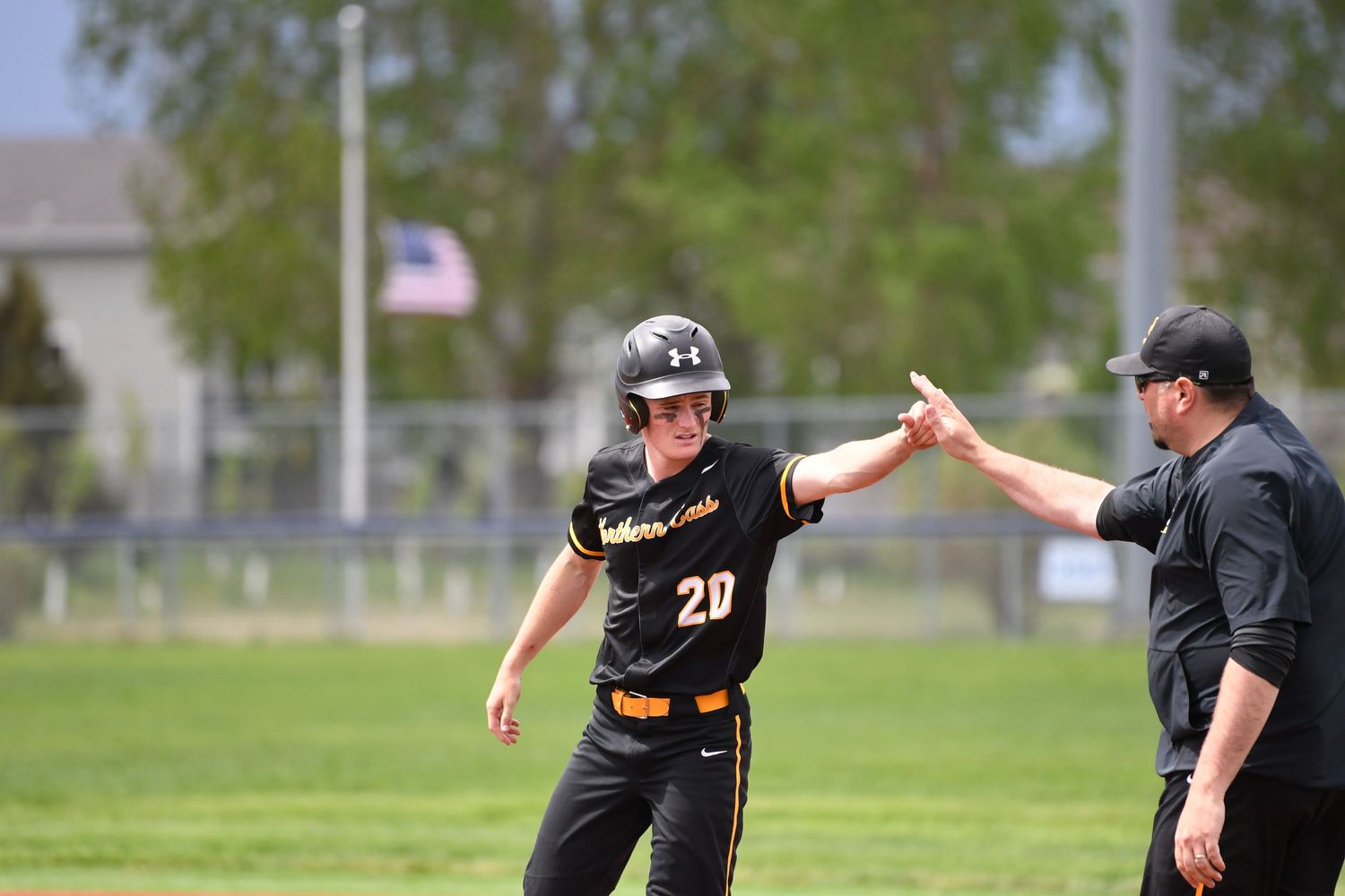 Baseball players in black uniforms compete during game on outdoor field with brick building in background.