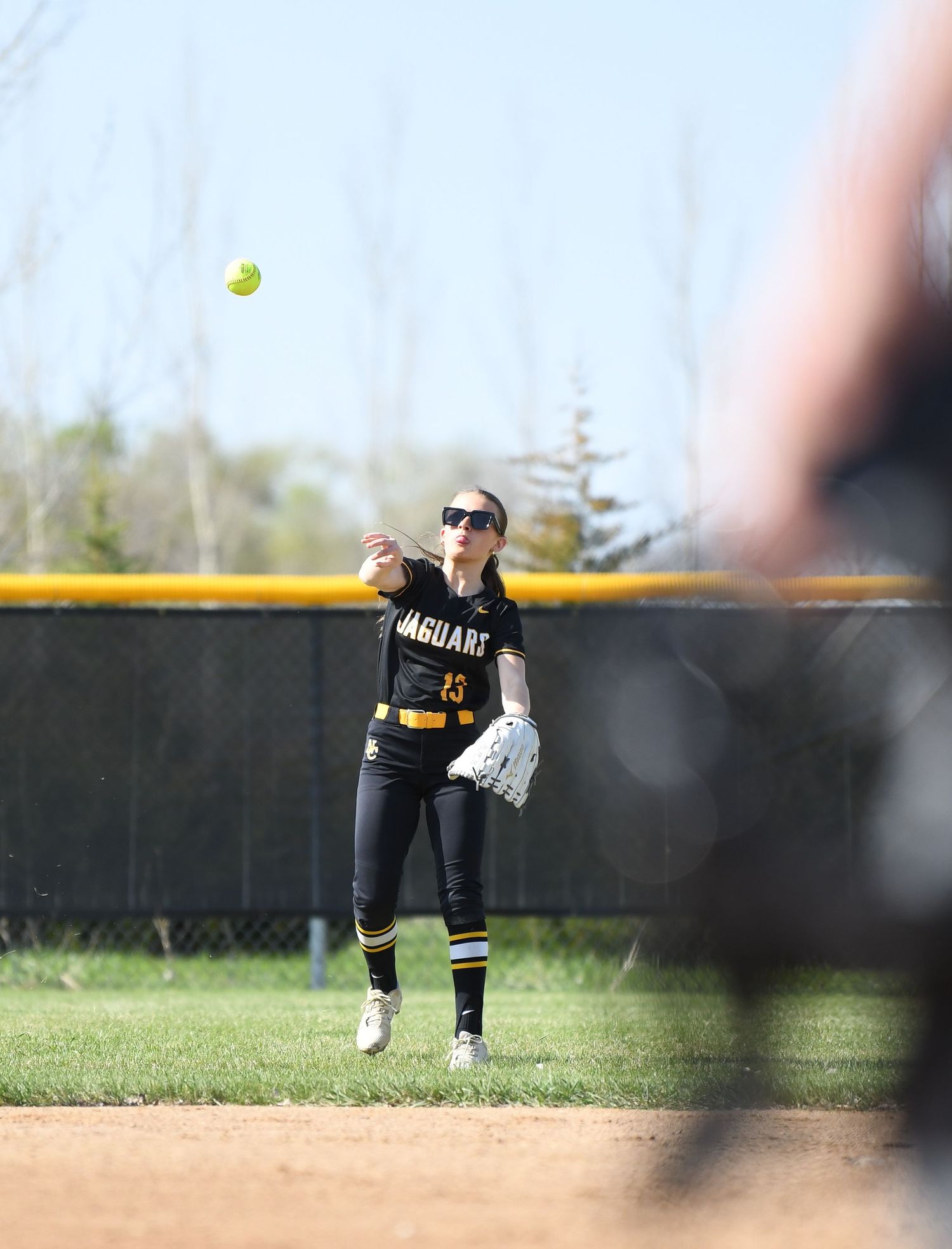 Softball player reaches to catch high ball in outfield during game.