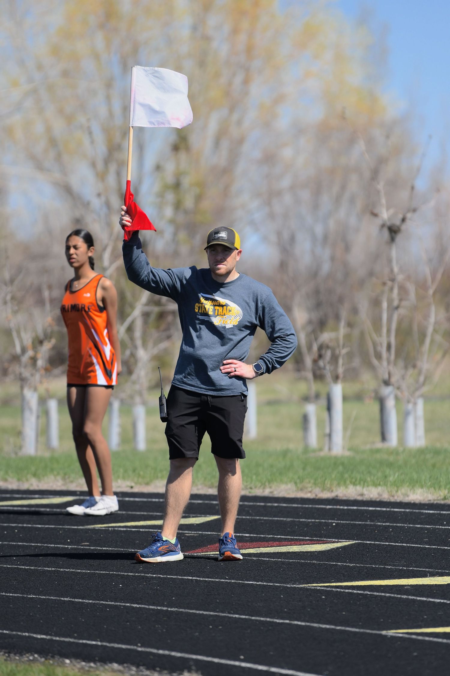 Track official holds up a white flag while standing on a track during an outdoor sporting event.
