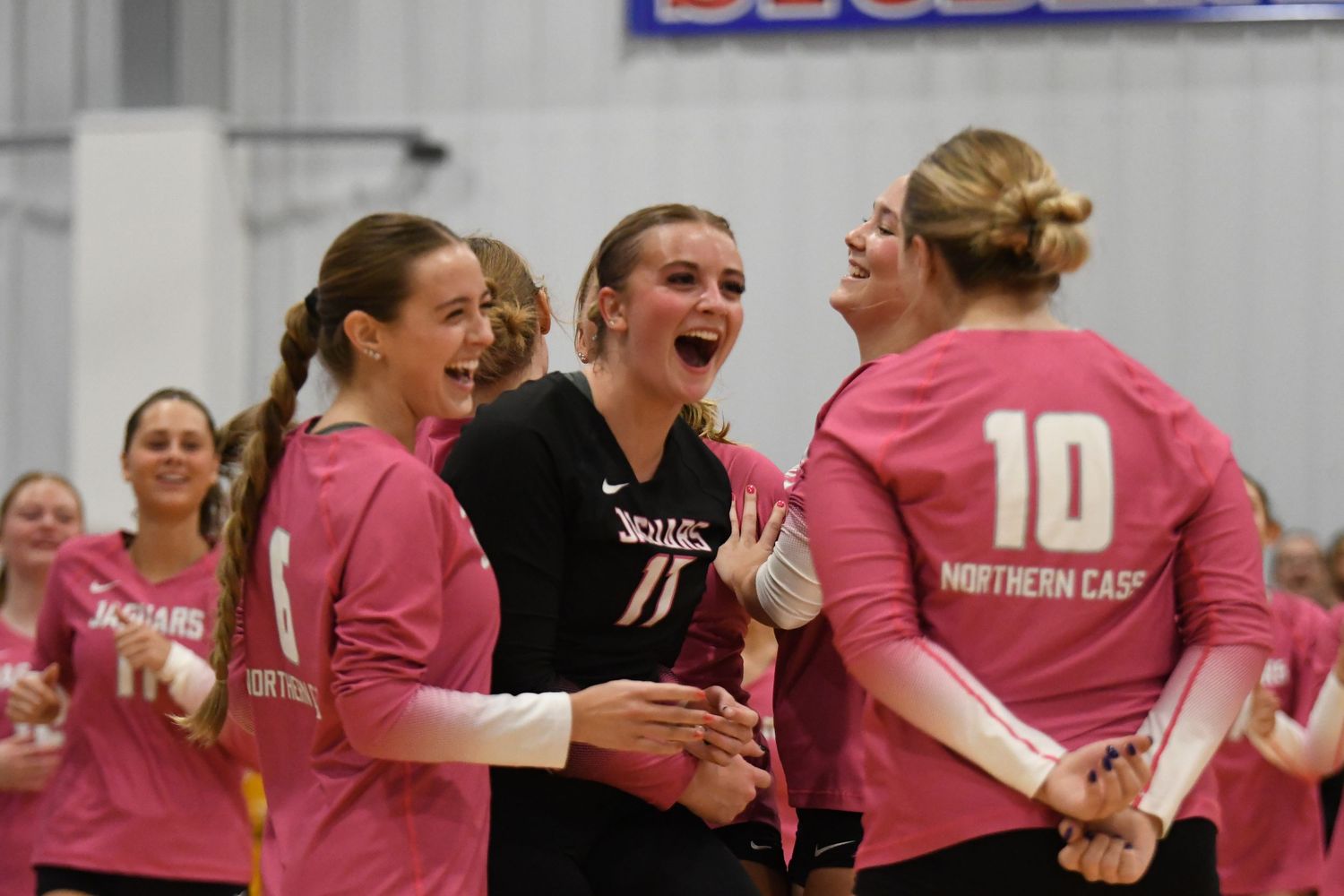 Players in pink jerseys celebrate joyfully on the sidelines of a volleyball match.