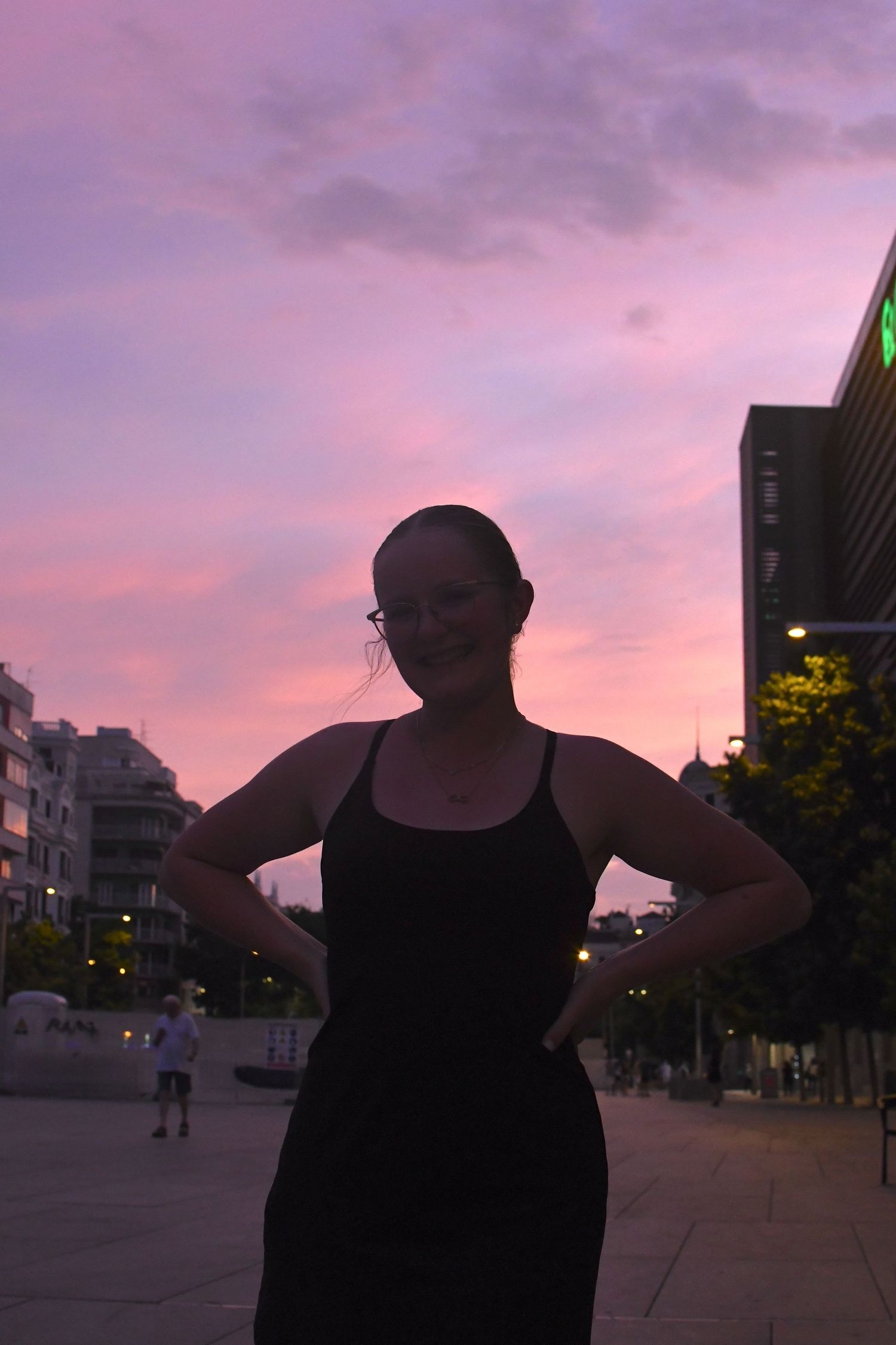 A silhouette stands against a vibrant purple sunset sky in an urban setting.