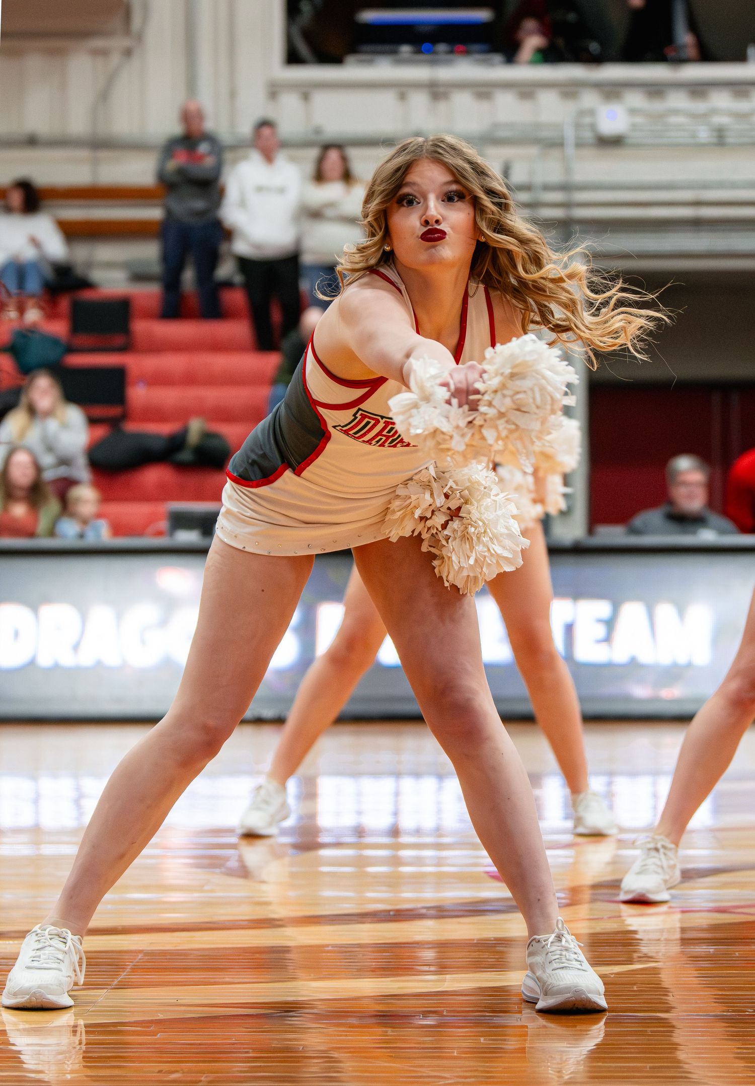 Cheerleaders perform a synchronized floor routine during a basketball game on the hardwood court.