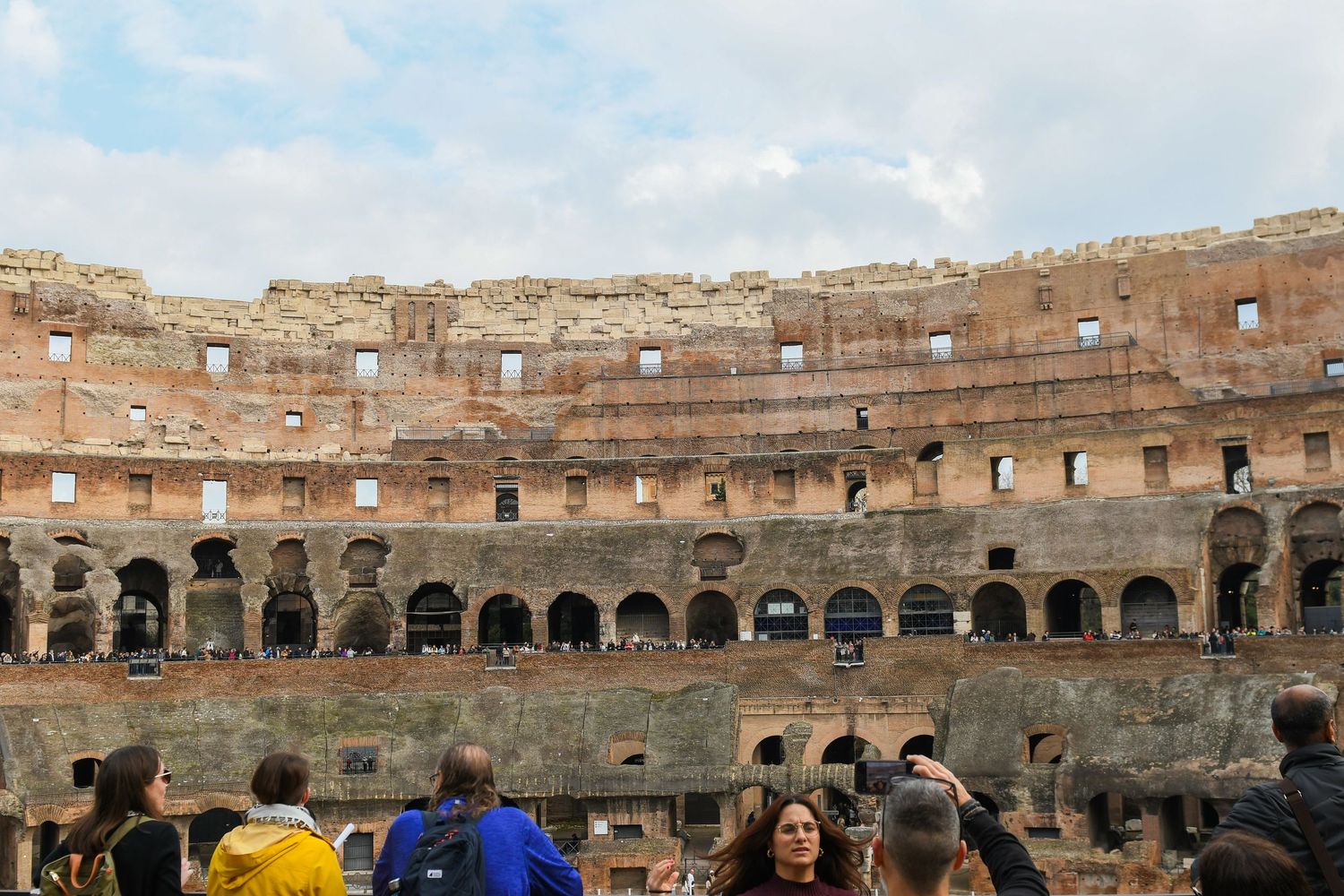 Ancient stone walls and arches of the Roman Colosseum interior with visitors viewing the historic amphitheater.