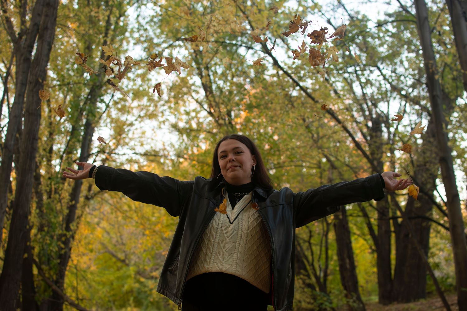 People with arms outstretched enjoying a beautiful autumn day in a forest with golden yellow leaves.