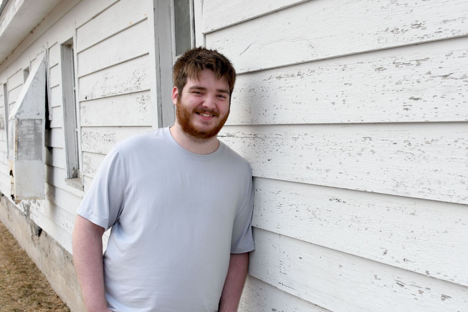 Casual outdoor portrait against white wooden siding background.