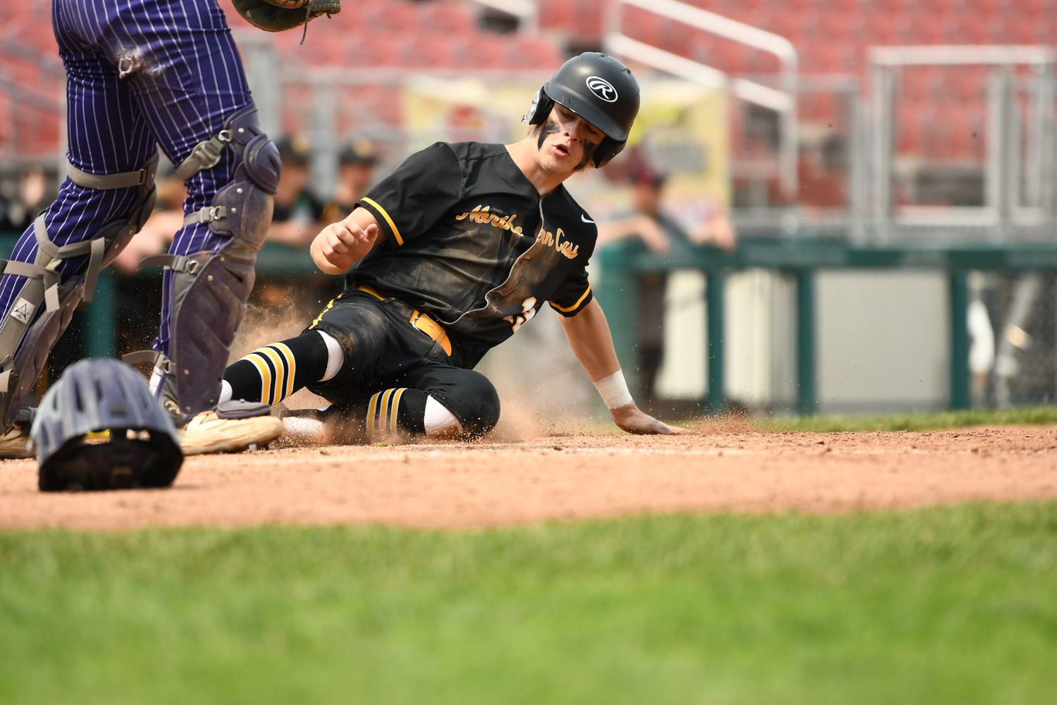Baseball player in black uniform slides into home plate during intense game action.