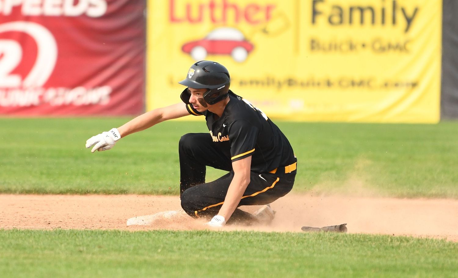 Baseball player in black uniform slides into base creating dust cloud during game.