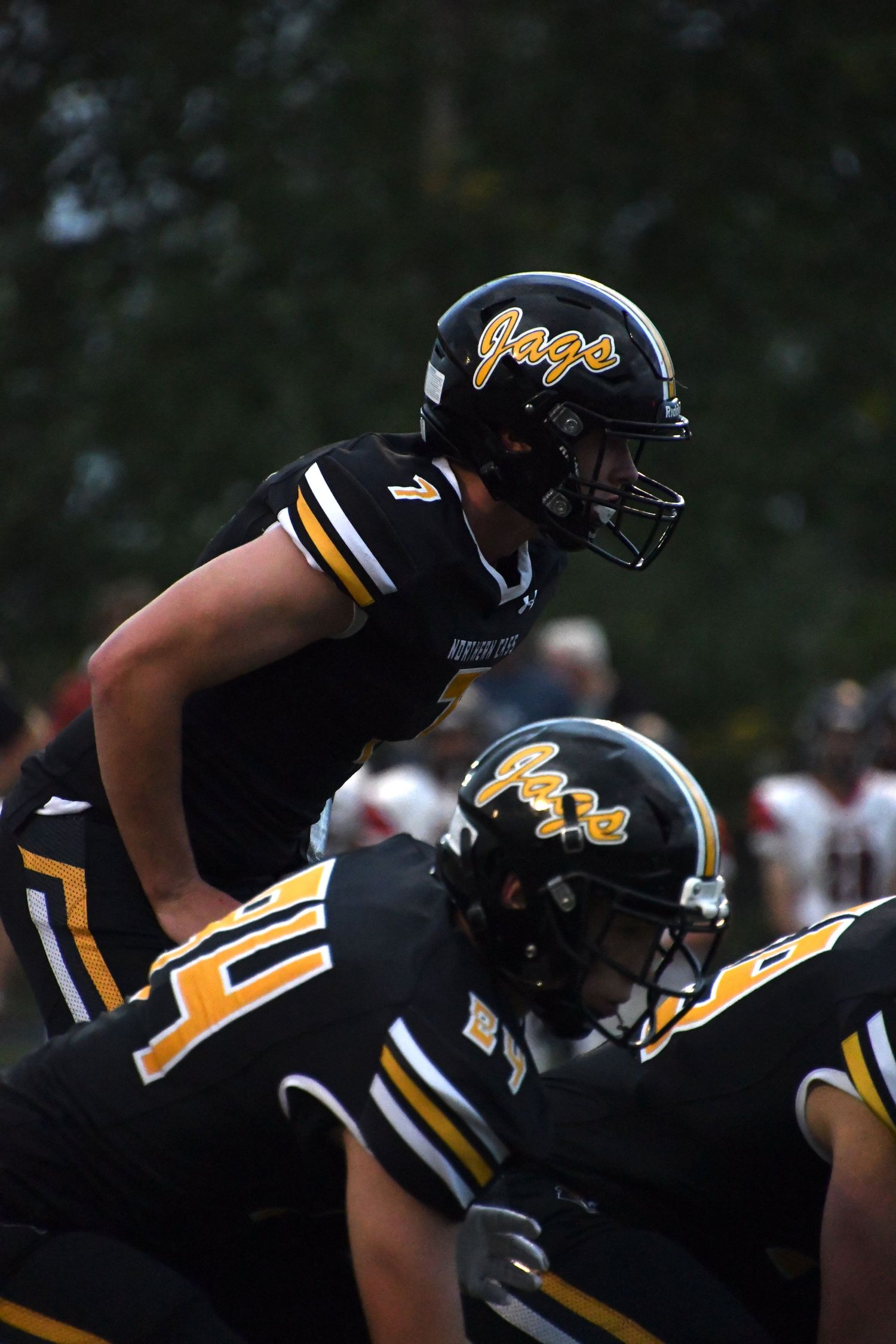 Football players wearing black and gold uniforms and helmets prepare for a play on the field.