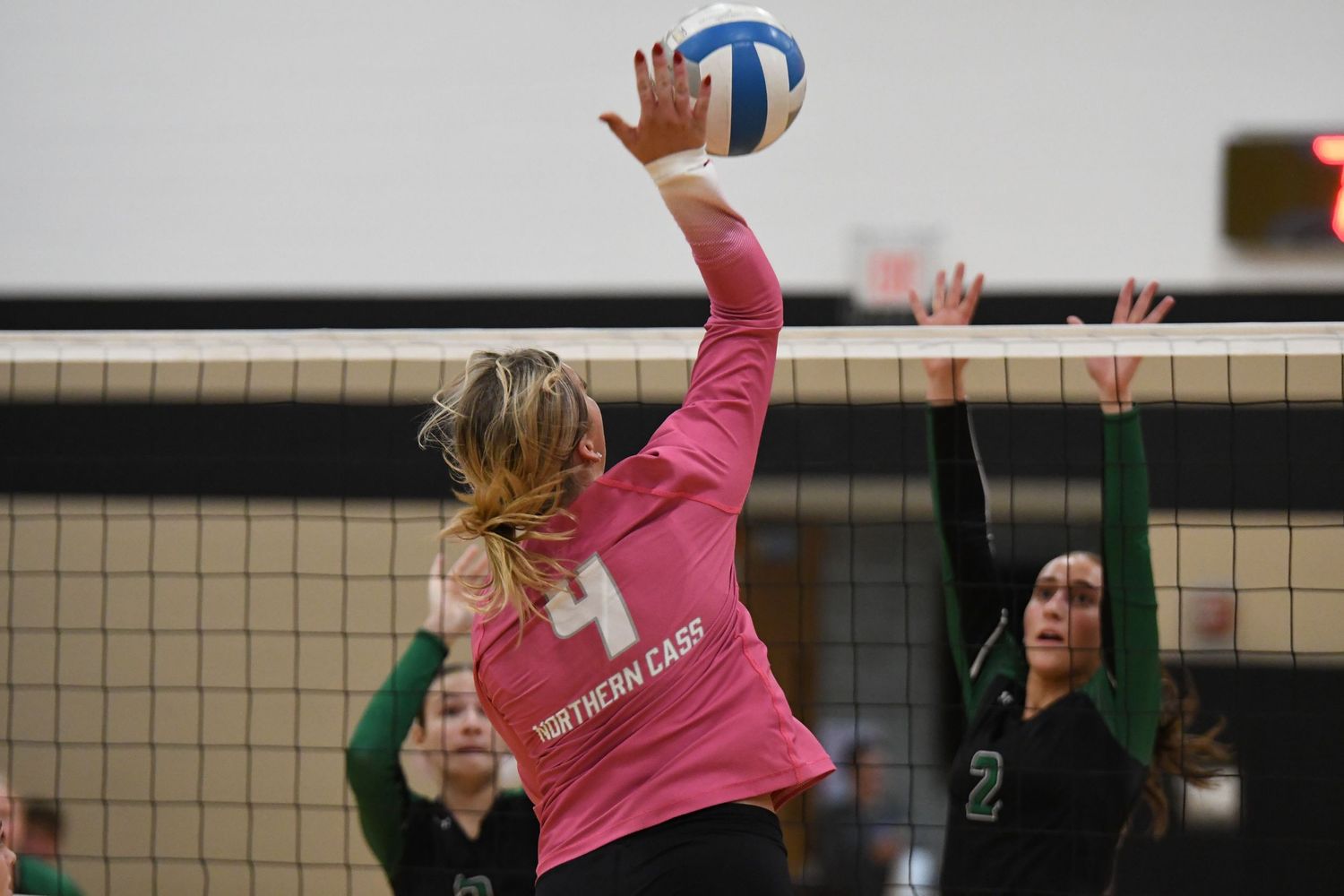 Volleyball players competing at net with one attempting a block against opponent's hit.