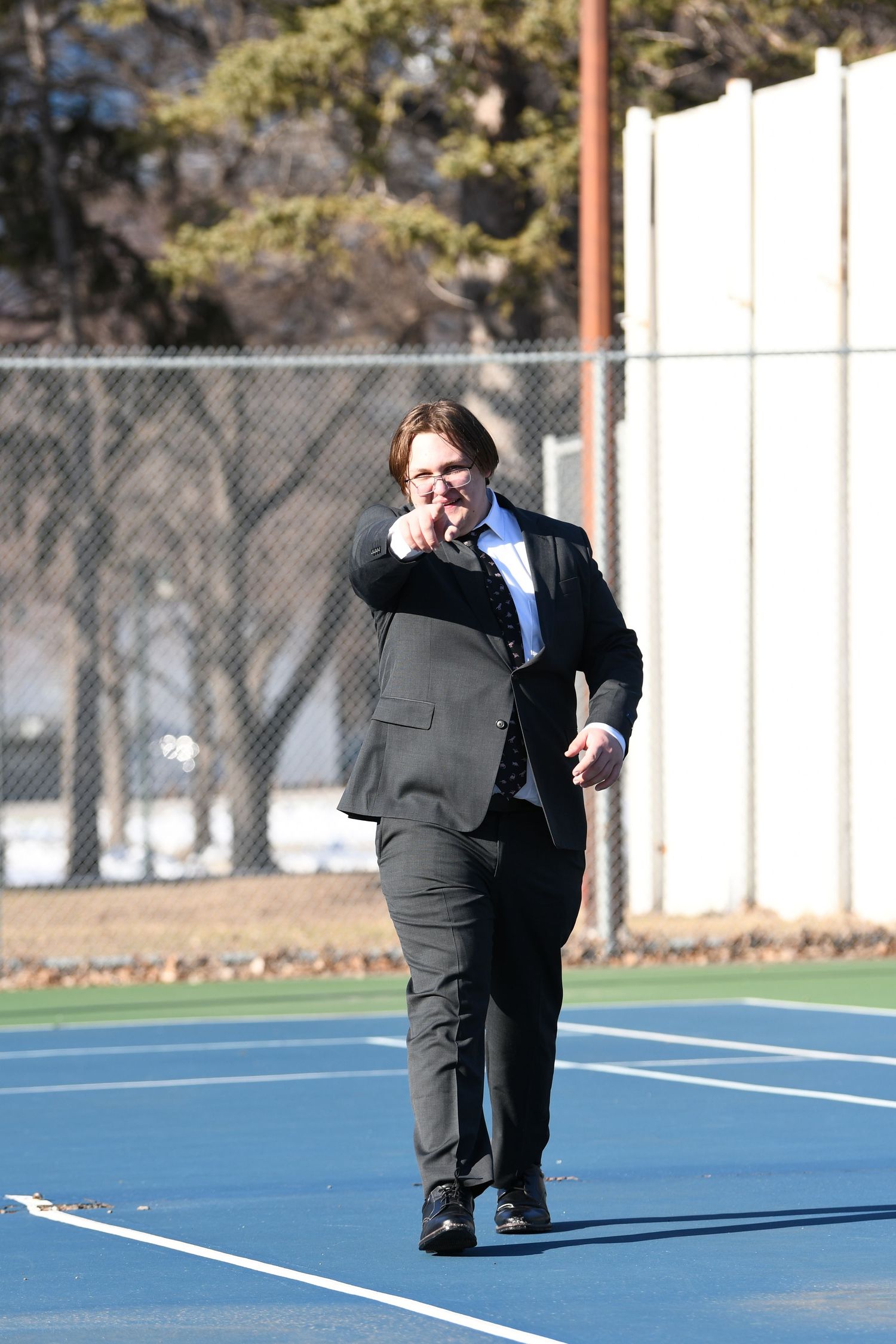 Person in business suit walking across blue sports court while talking on phone.