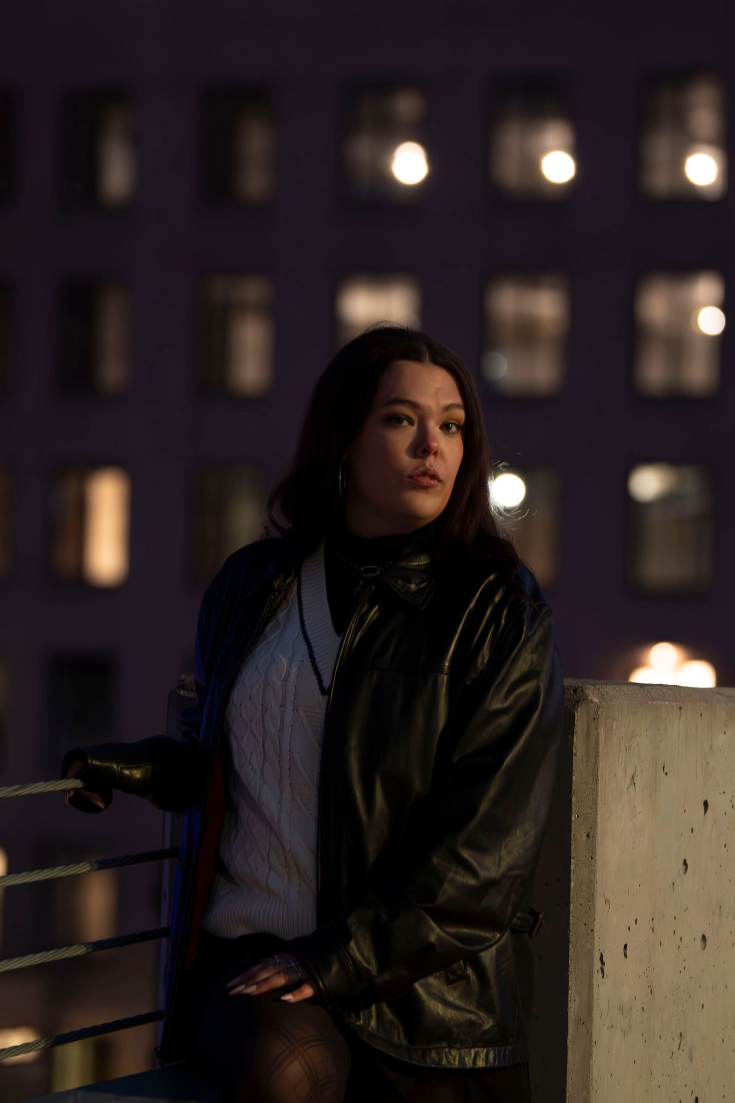 Nighttime urban portrait with city lights and illuminated windows creating a moody atmosphere.