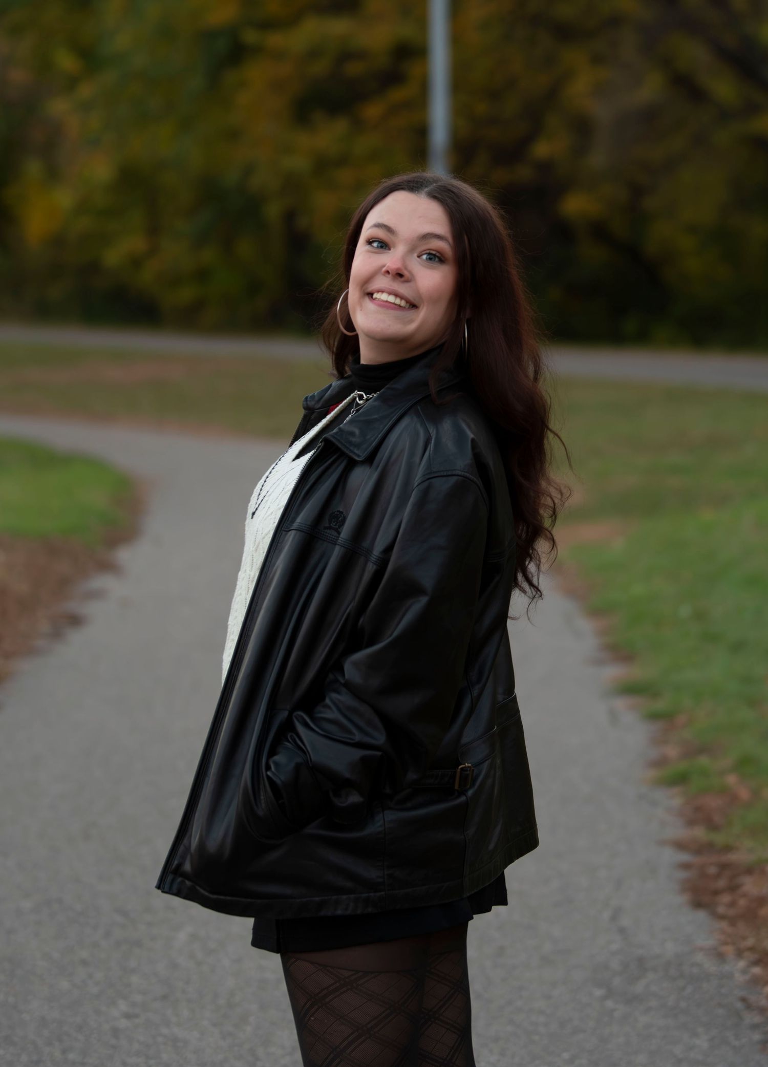Figure in black jacket twirls playfully on path surrounded by fall foliage.