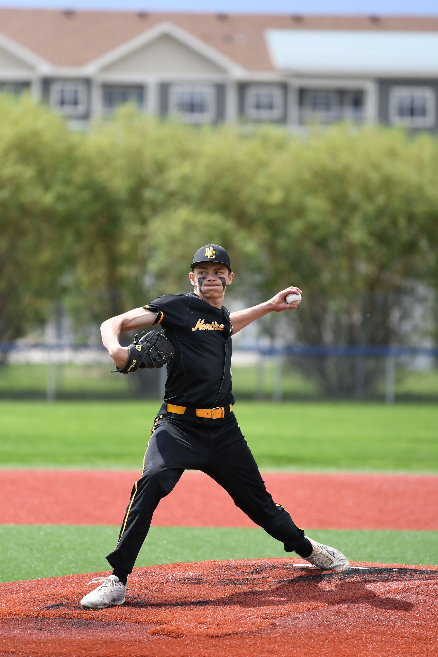 Baseball pitcher in mid-delivery wearing black uniform on the pitcher's mound.