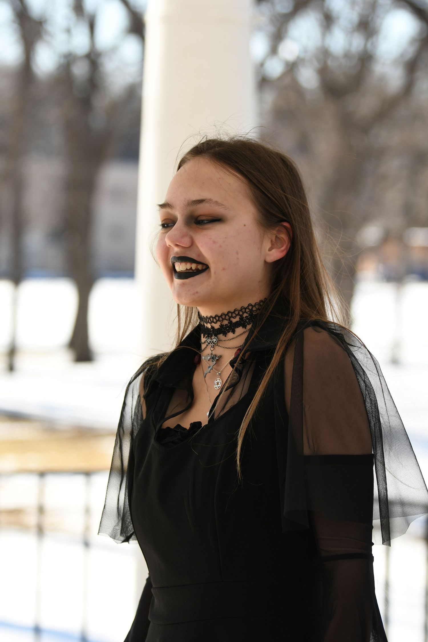 Woman in gothic black dress smiles outdoors in a winter landscape.