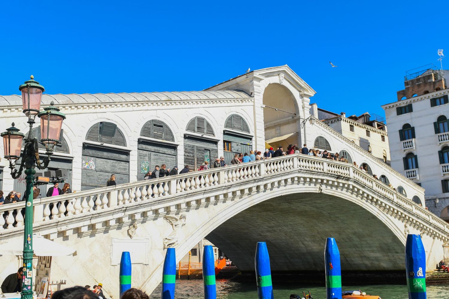 Panoramic view of Venice's iconic Rialto Bridge spanning the Grand Canal with traditional buildings and blue skies.