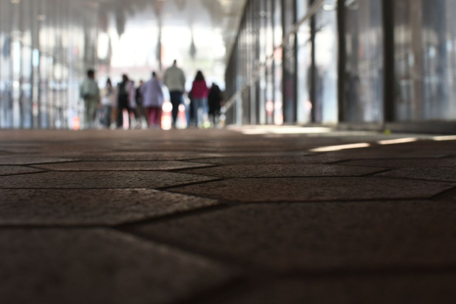 Blurred figures walk through a corridor with dramatic lighting and shadows on the floor.