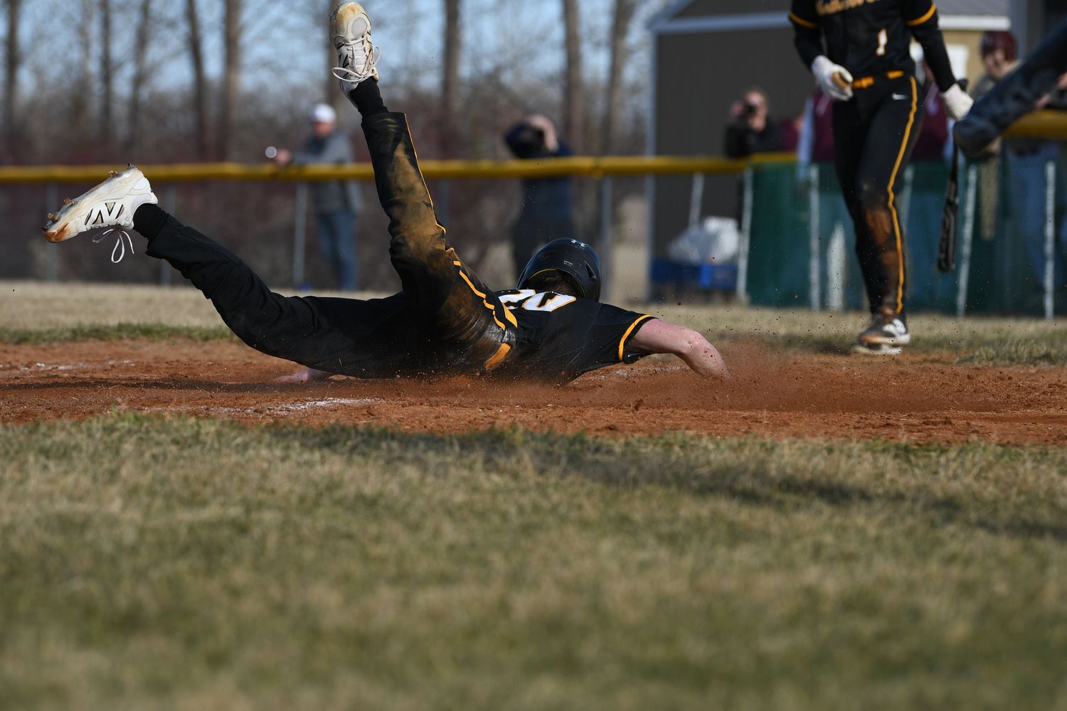 Baseball player in black uniform slides dramatically across baseball field during game.