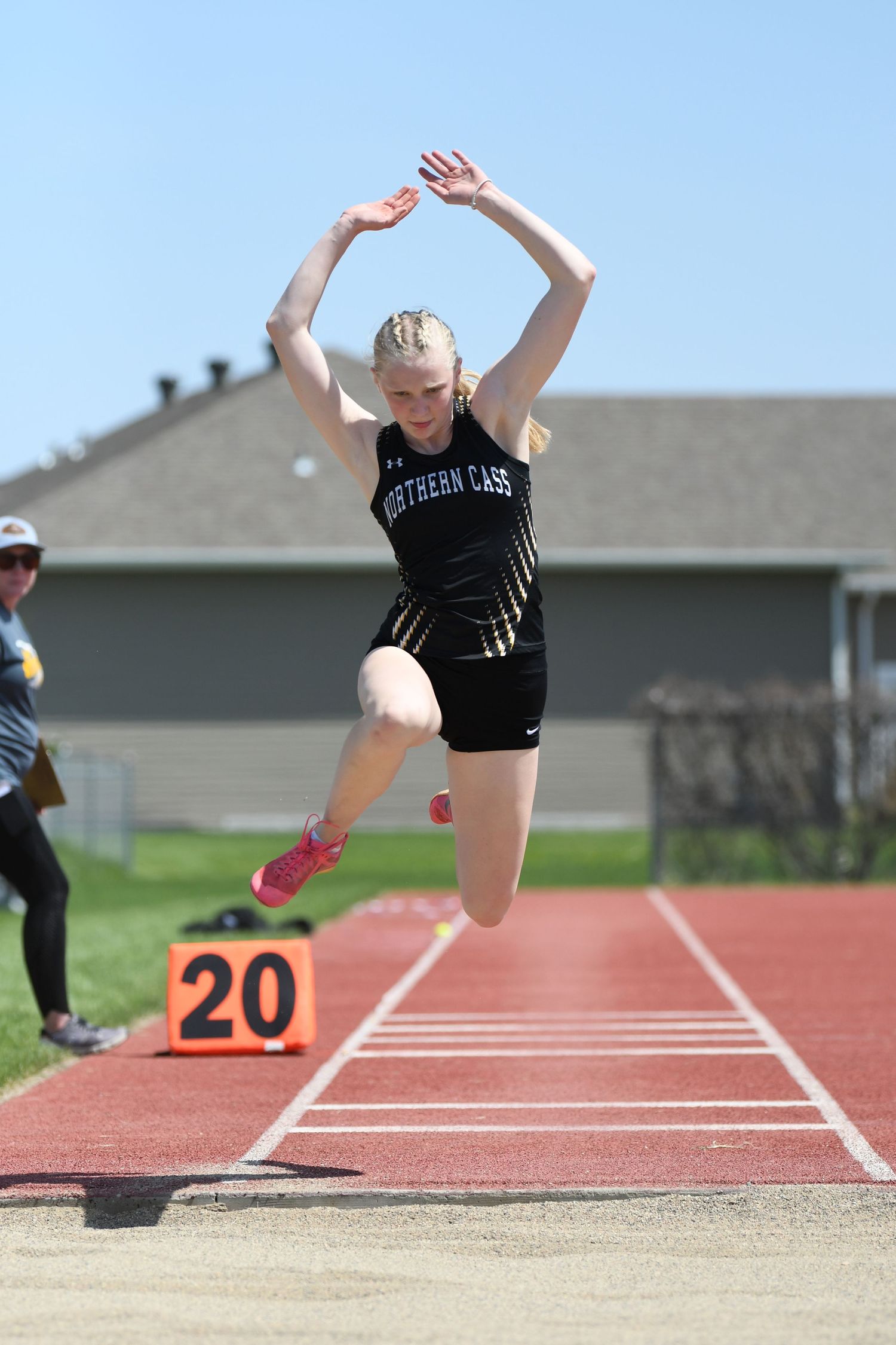 Athlete performs long jump on outdoor track with landing pit marked as 20.
