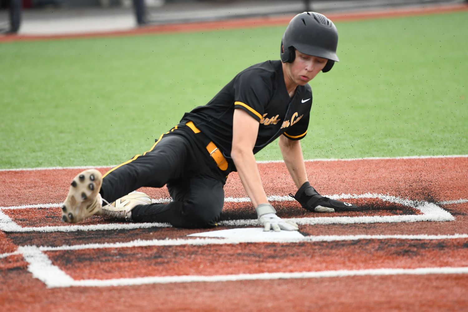 Baseball player slides into base on the red turf field.