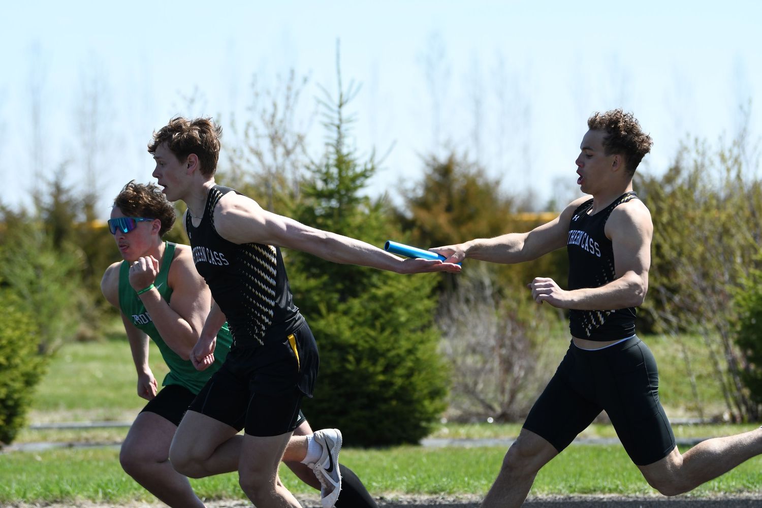 Athletes passing baton during relay race on sunny track field.