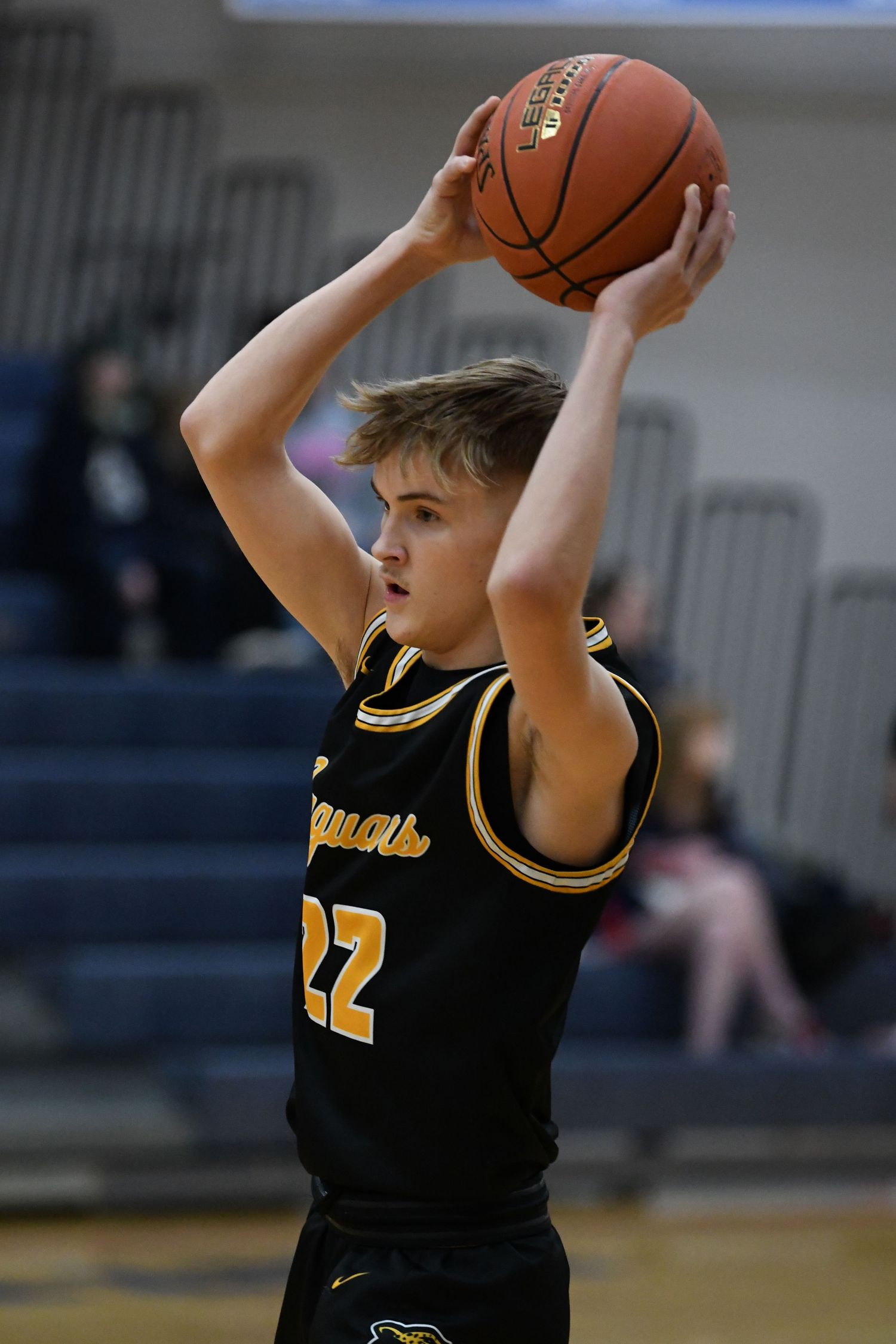 Basketball player in black jersey number 22 holds ball overhead during high school game.