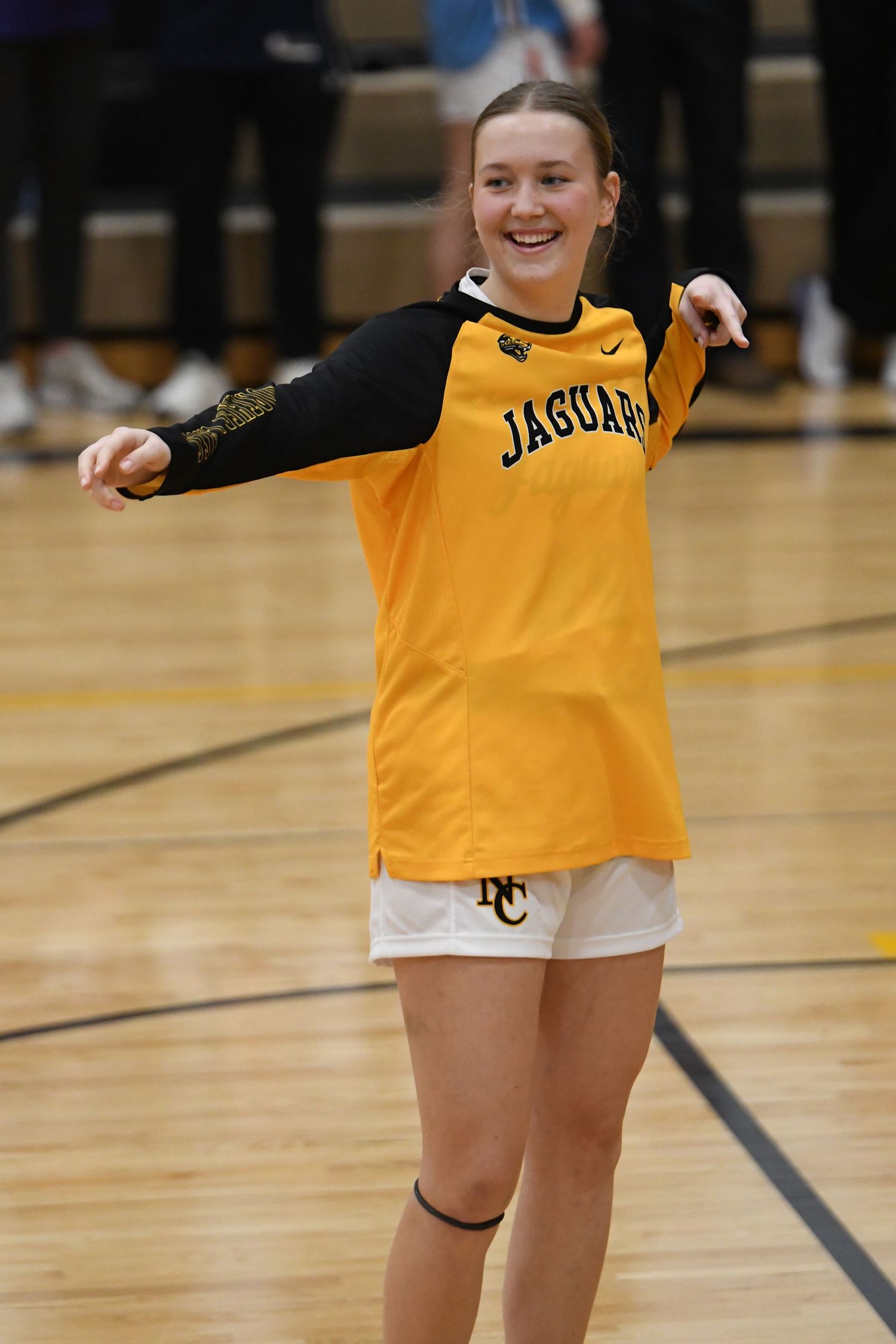 Player in yellow Jaguars warmup jersey smiling on basketball court during practice.