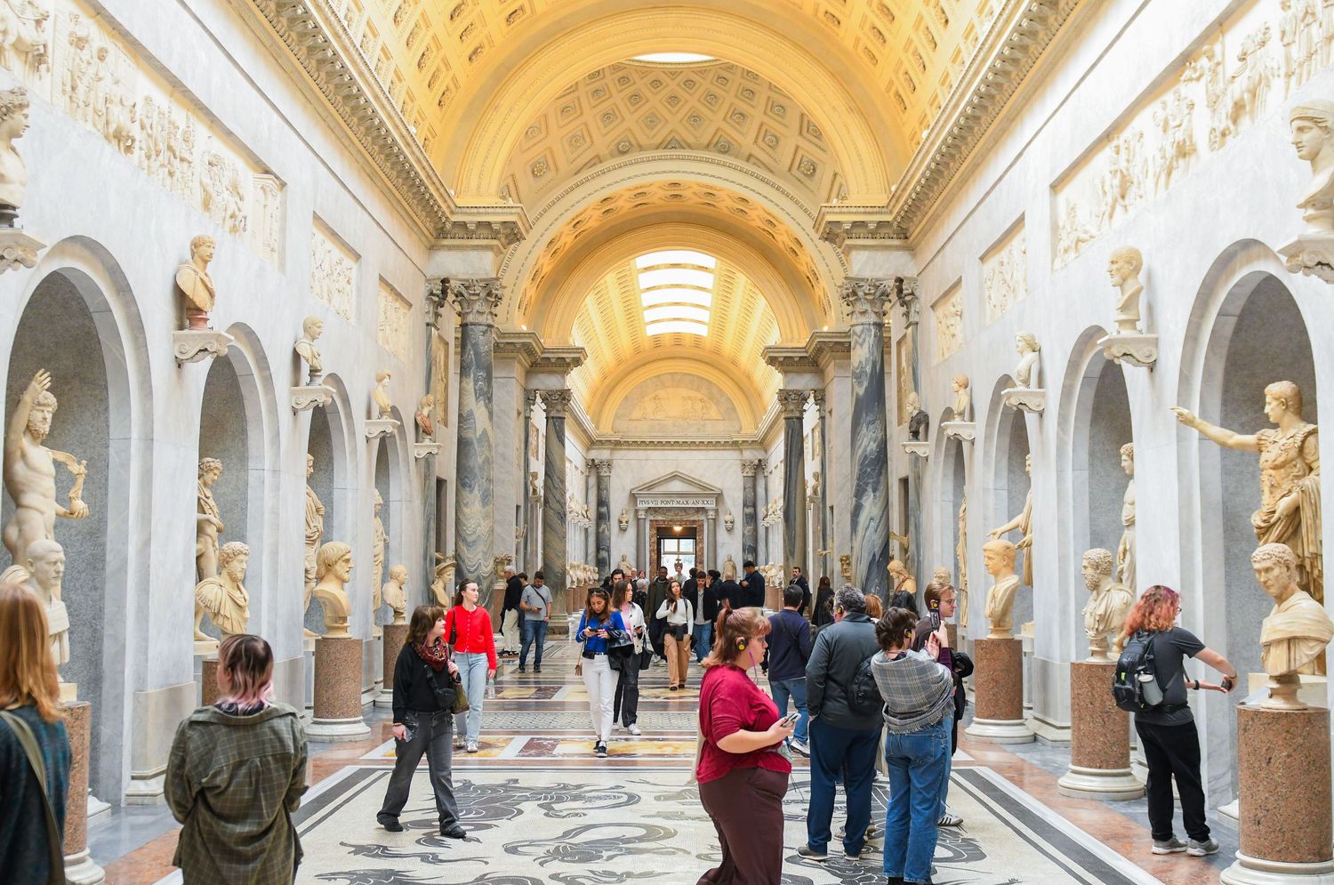 Elegant museum corridor with vaulted ceiling and classical sculptures along the walls.