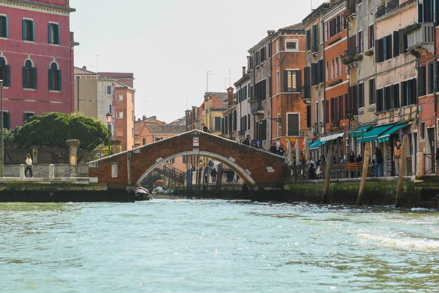 A picturesque Venice canal with traditional brick bridge and colorful Italian buildings along the waterfront.